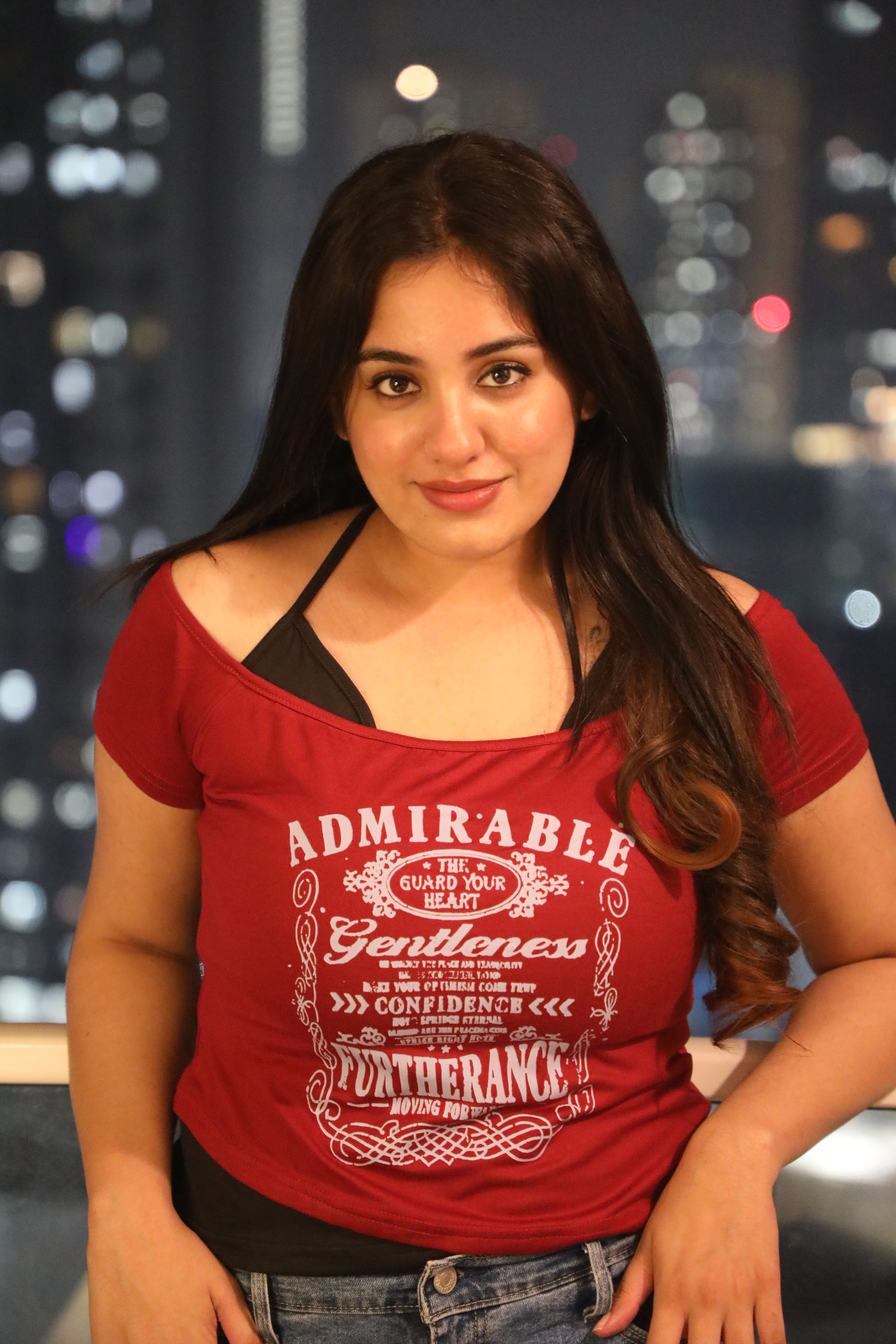 Portrait of a young woman wearing a red top with night cityscape in the background.