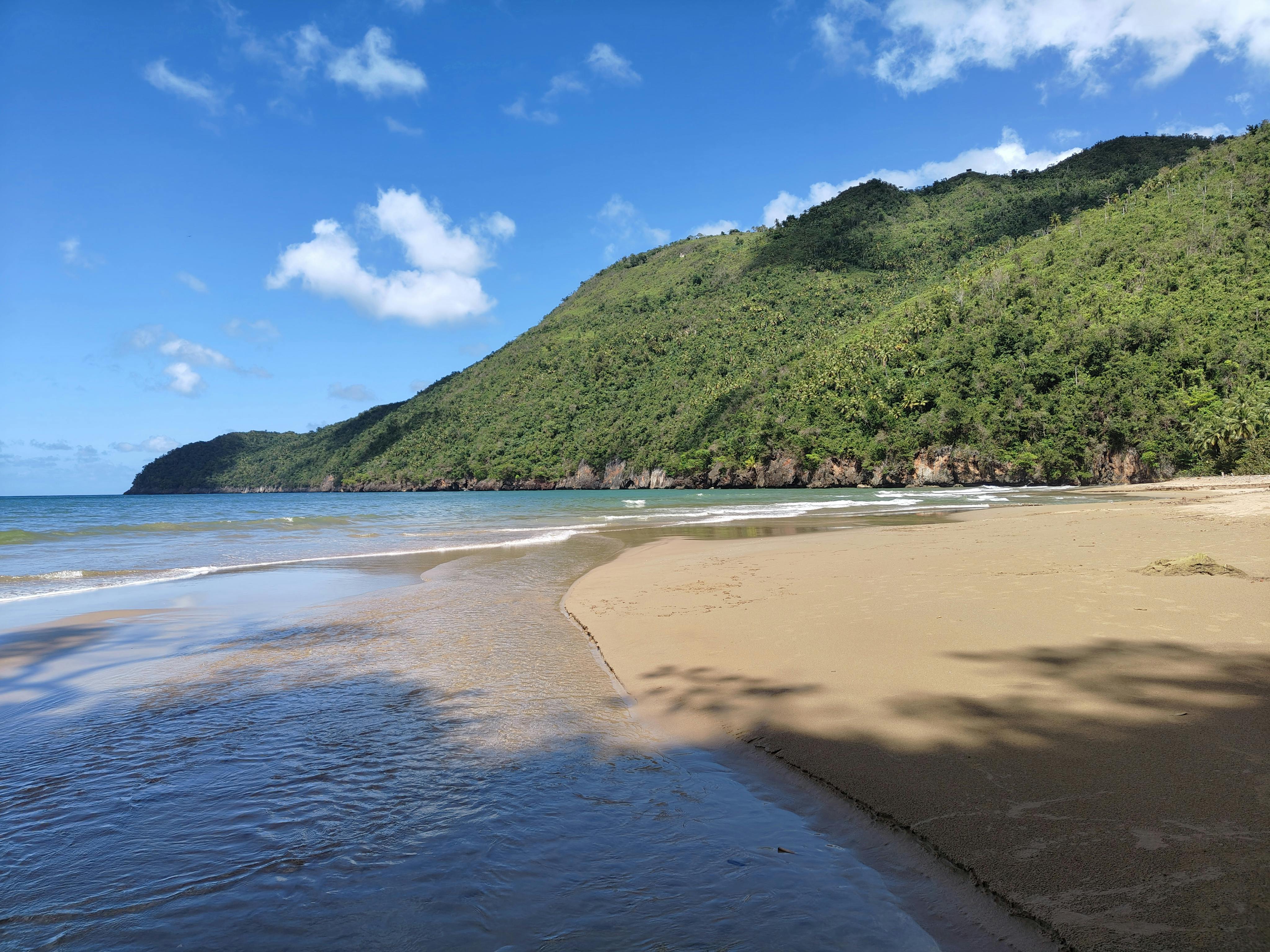Kostnadsfria En lugn tropisk strand med gyllene sand och frodiga gröna kullar under en vibrerande blå himmel. Stock foto