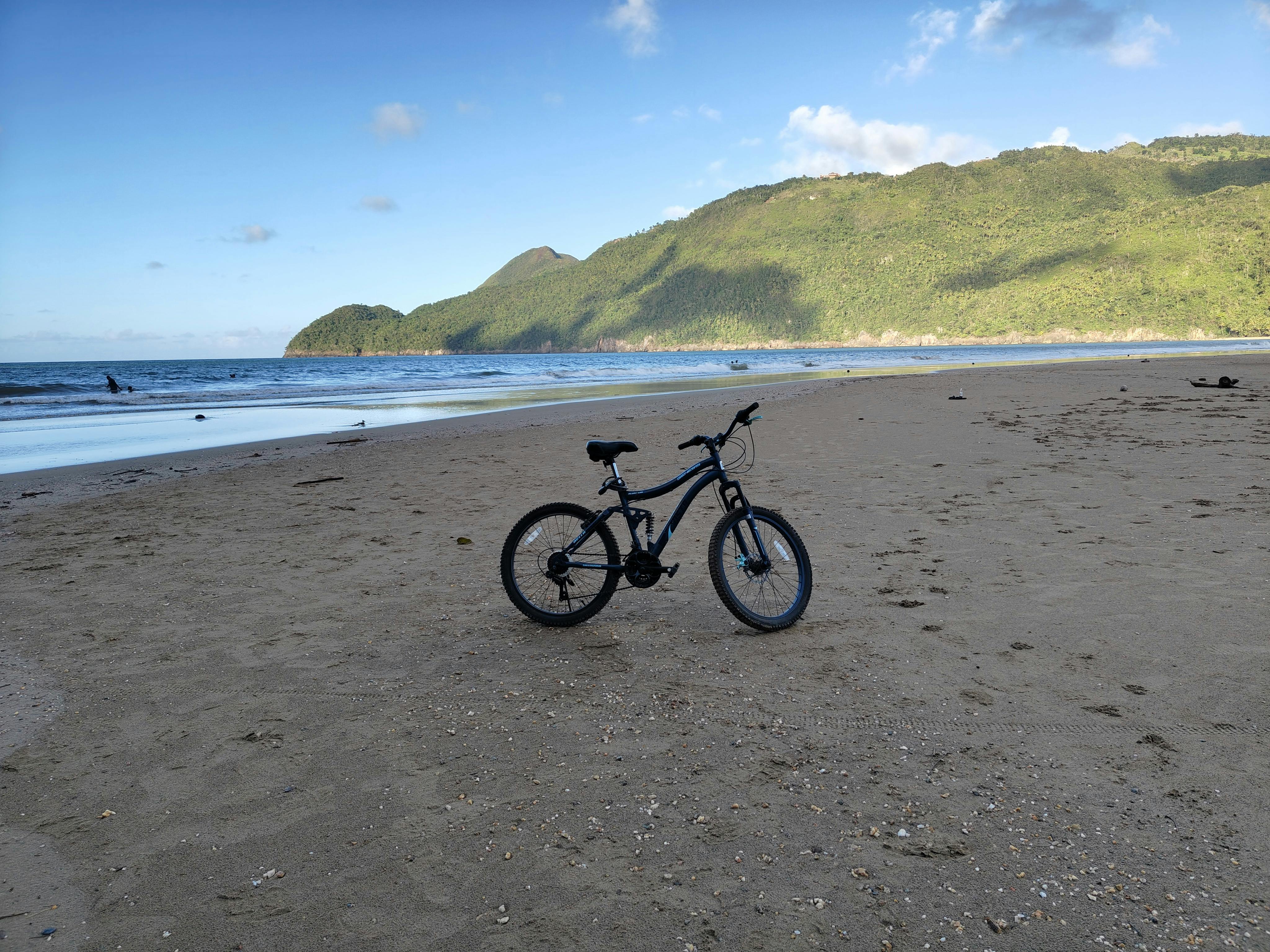 Kostnadsfria En cykel vilar på en sandstrand med berg och hav i bakgrunden. Stock foto