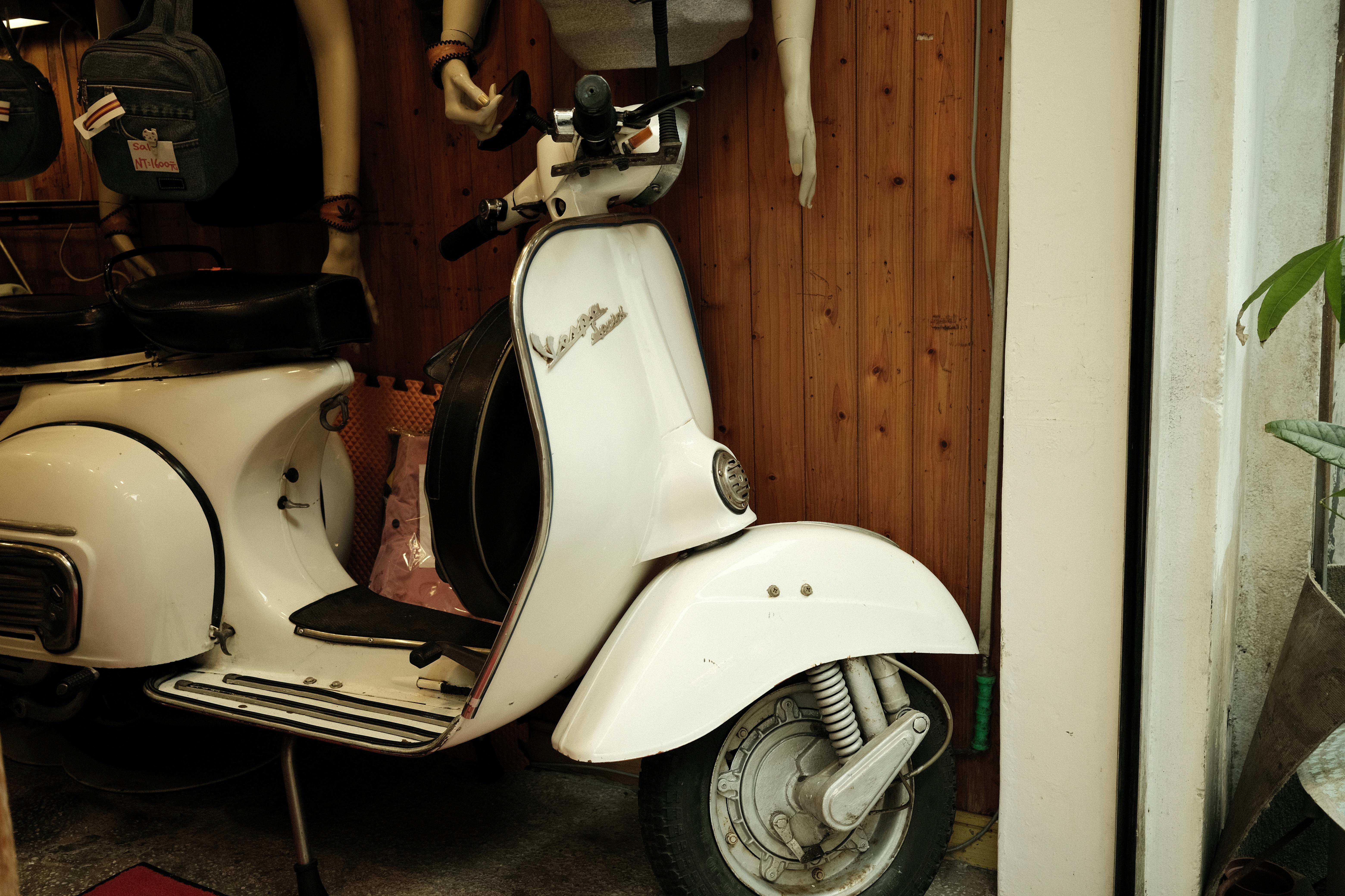 Vintage white scooter displayed indoors with mannequins and accessories.