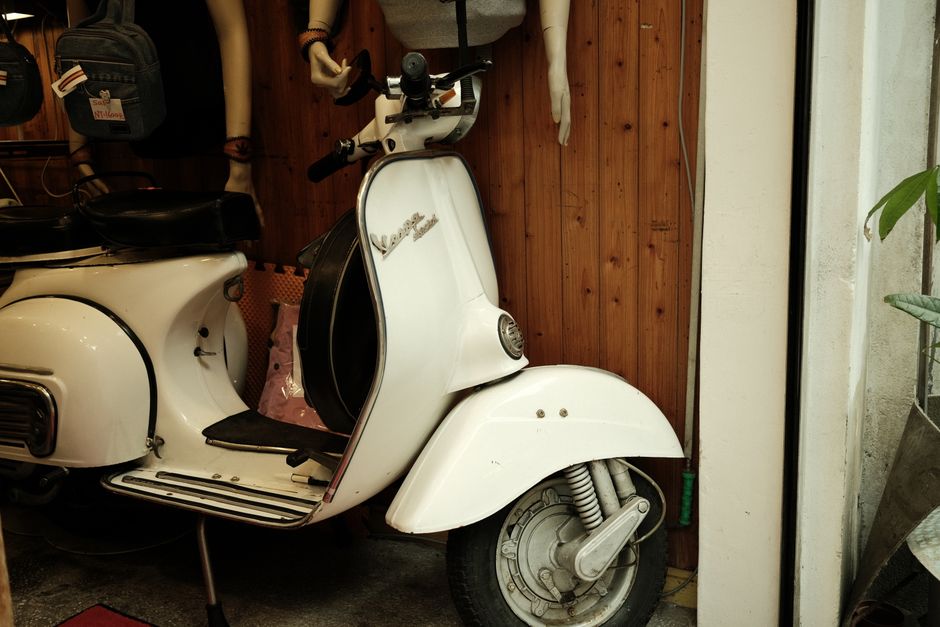 Vintage white scooter displayed indoors with mannequins and accessories.