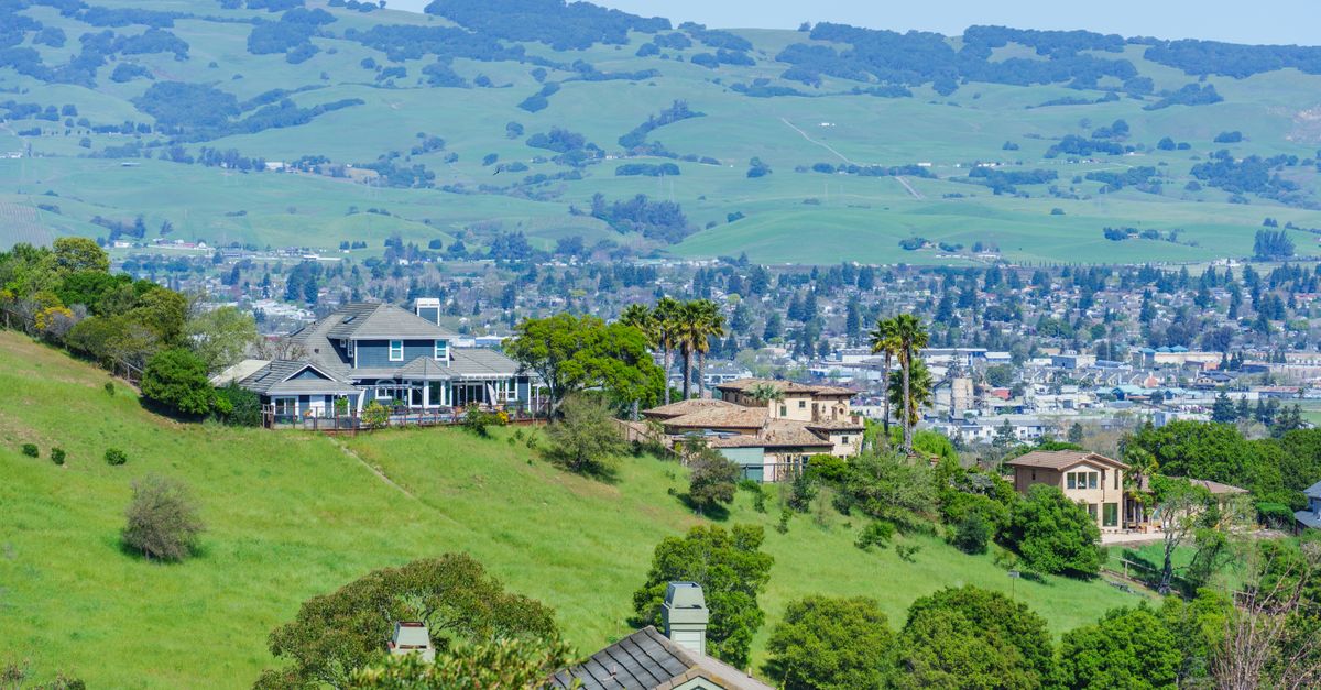 Charming hillside houses with lush green surroundings, overlooking a sprawling valley on a sunny day.