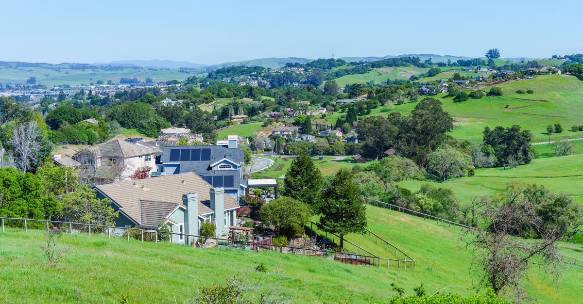 Picturesque suburban neighborhood with lush green hills and clear blue skies, showcasing a peaceful, idyllic lifestyle.