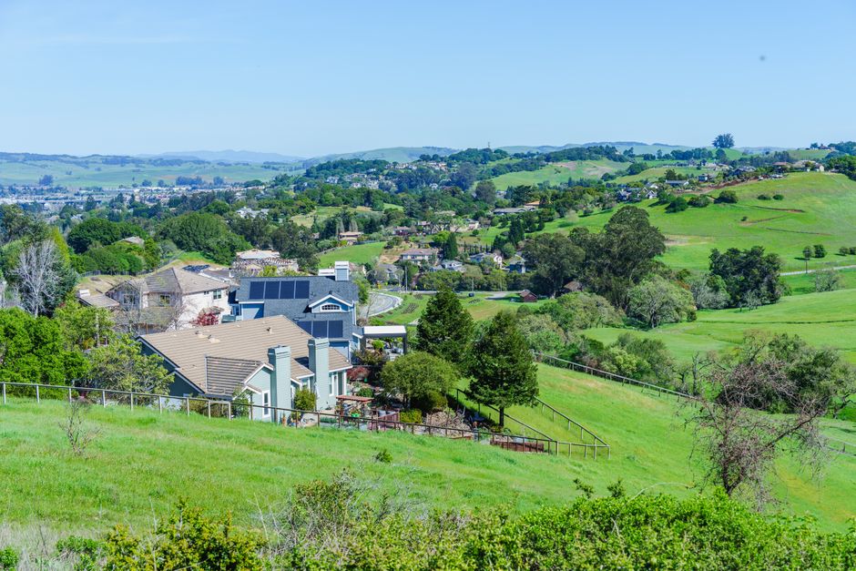Picturesque suburban neighborhood with lush green hills and clear blue skies, showcasing a peaceful, idyllic lifestyle.