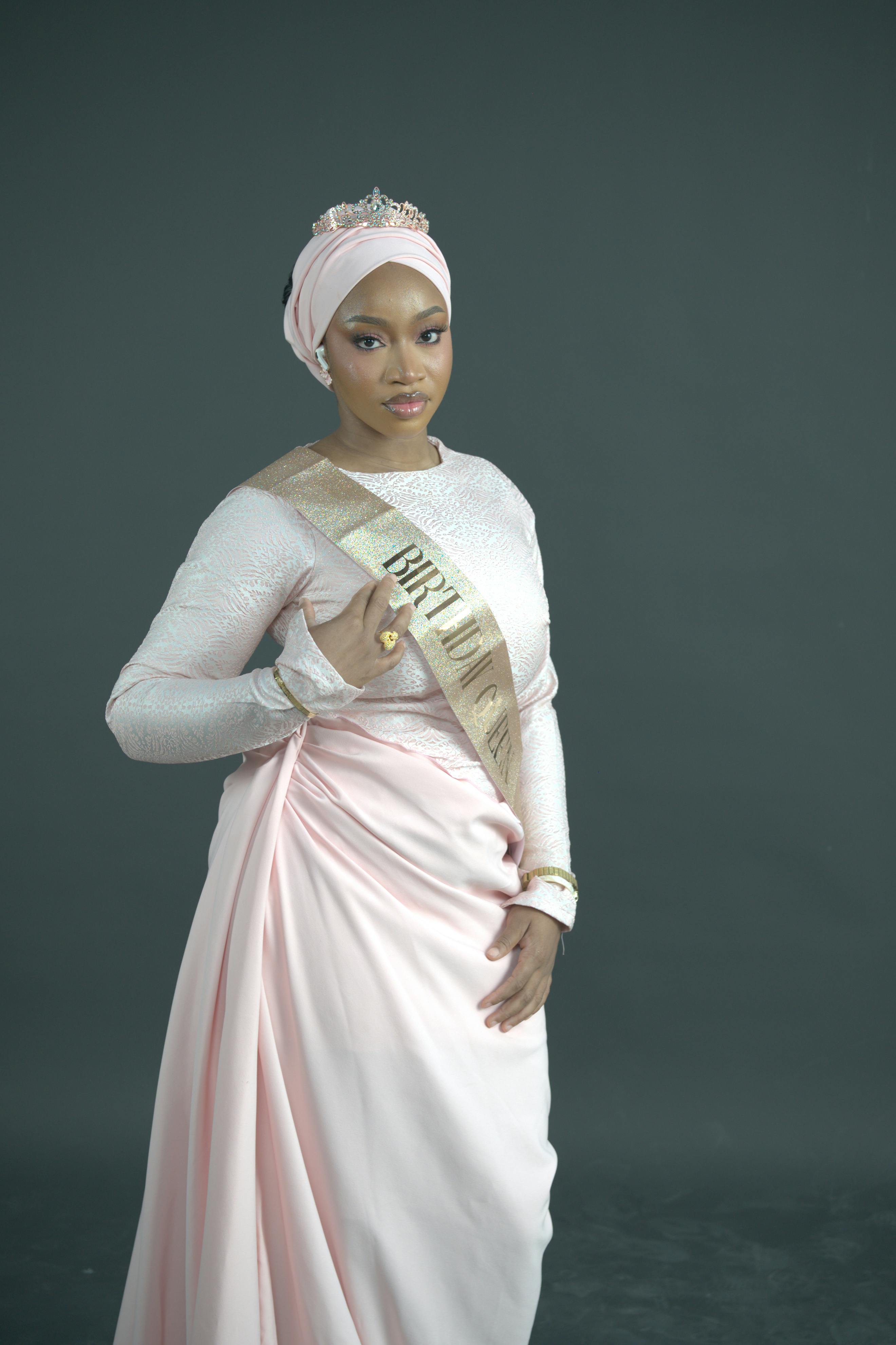 Portrait of an elegant woman wearing a traditional pink dress and a sash against a dark background.