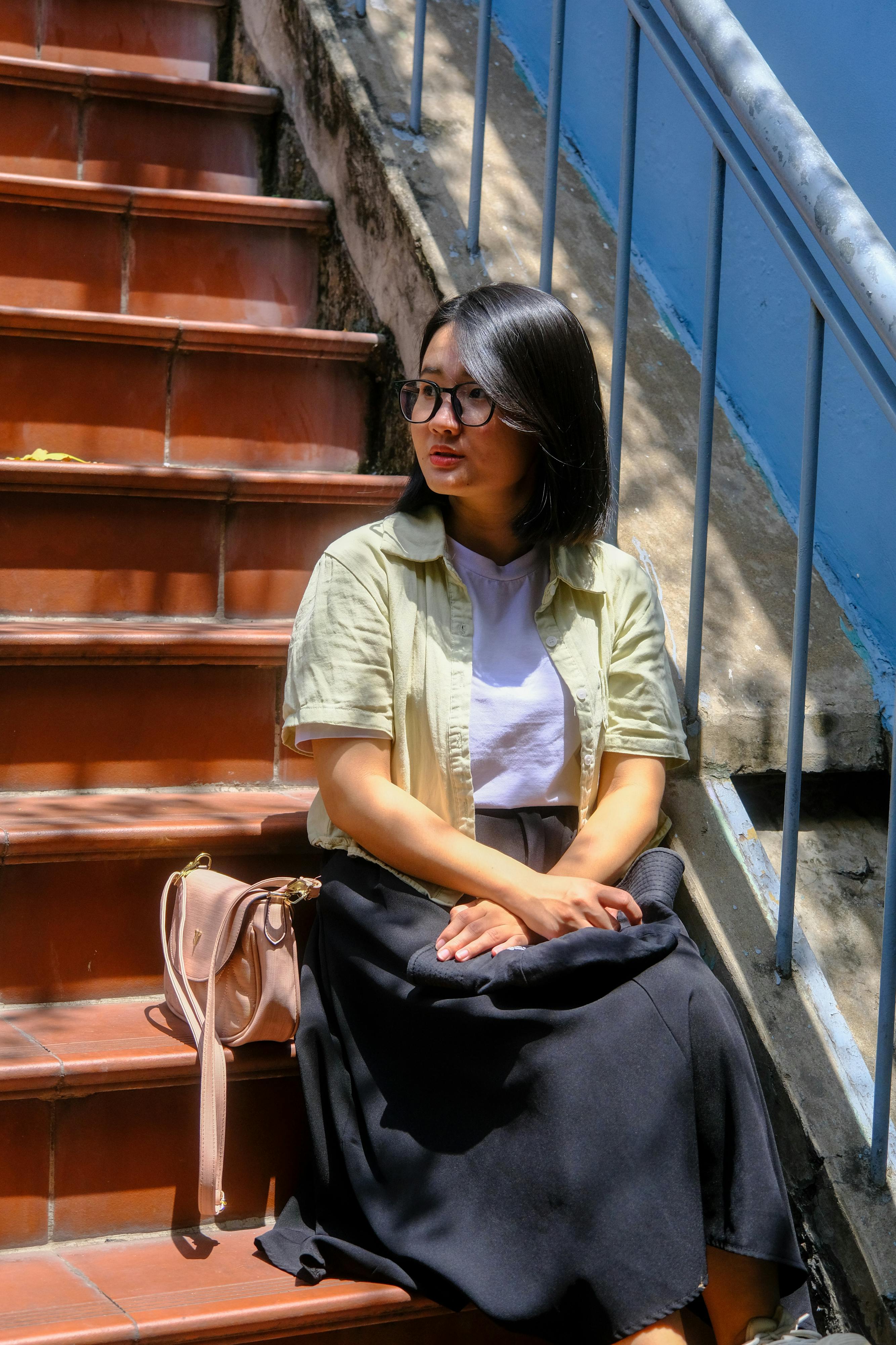 Gratuit Portrait d'une femme pensive assise sur des marches en terre cuite à Hué, au Vietnam, la lumière du soleil projetant de douces ombres. Photos