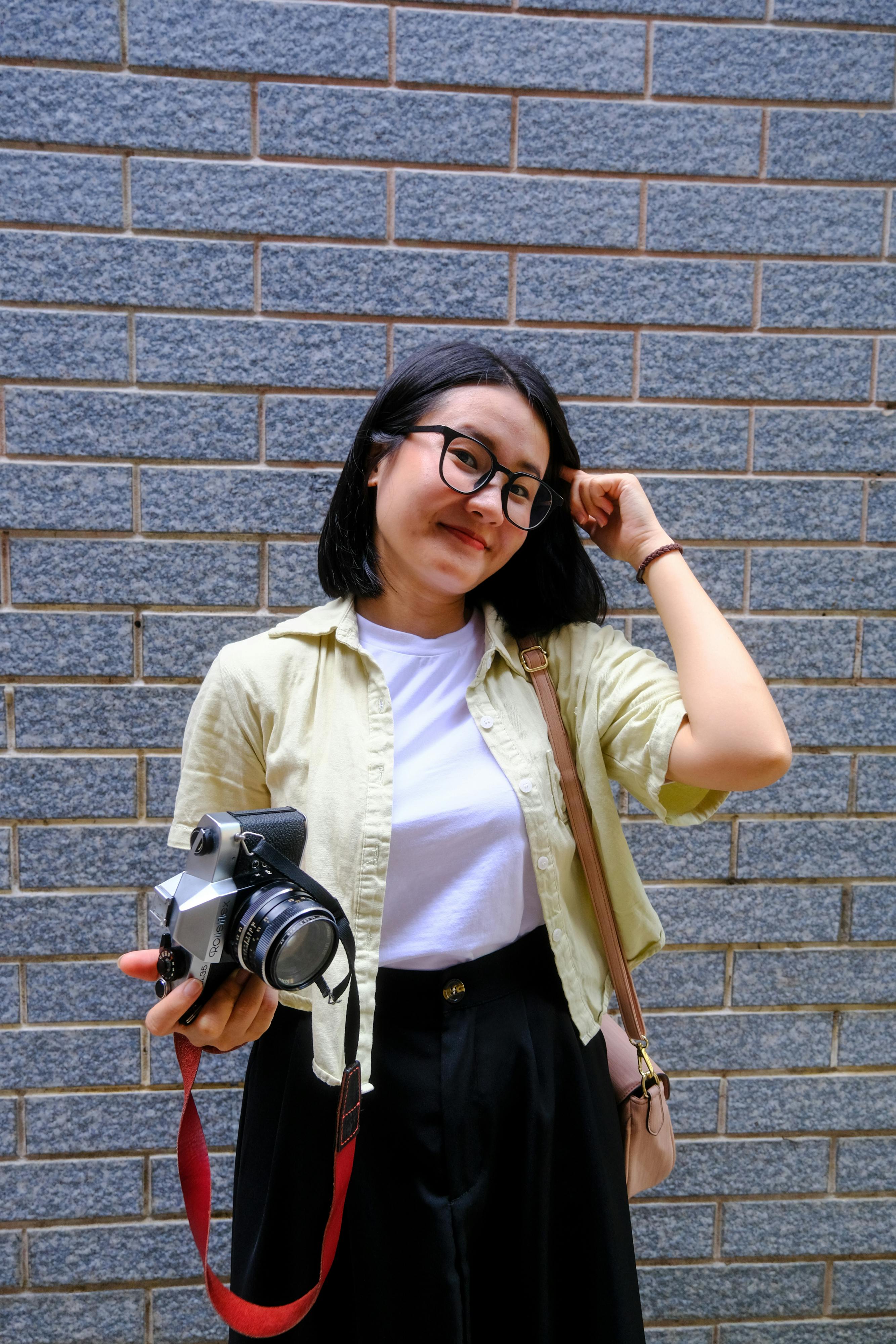 bezplatná Usmívající se žena s kamerou stojící u cihlové zdi v Hue, Vietnam. Základová fotografie