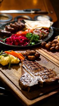 Delicious T-bone steak served with roasted vegetables and mushrooms on a wooden platter.
