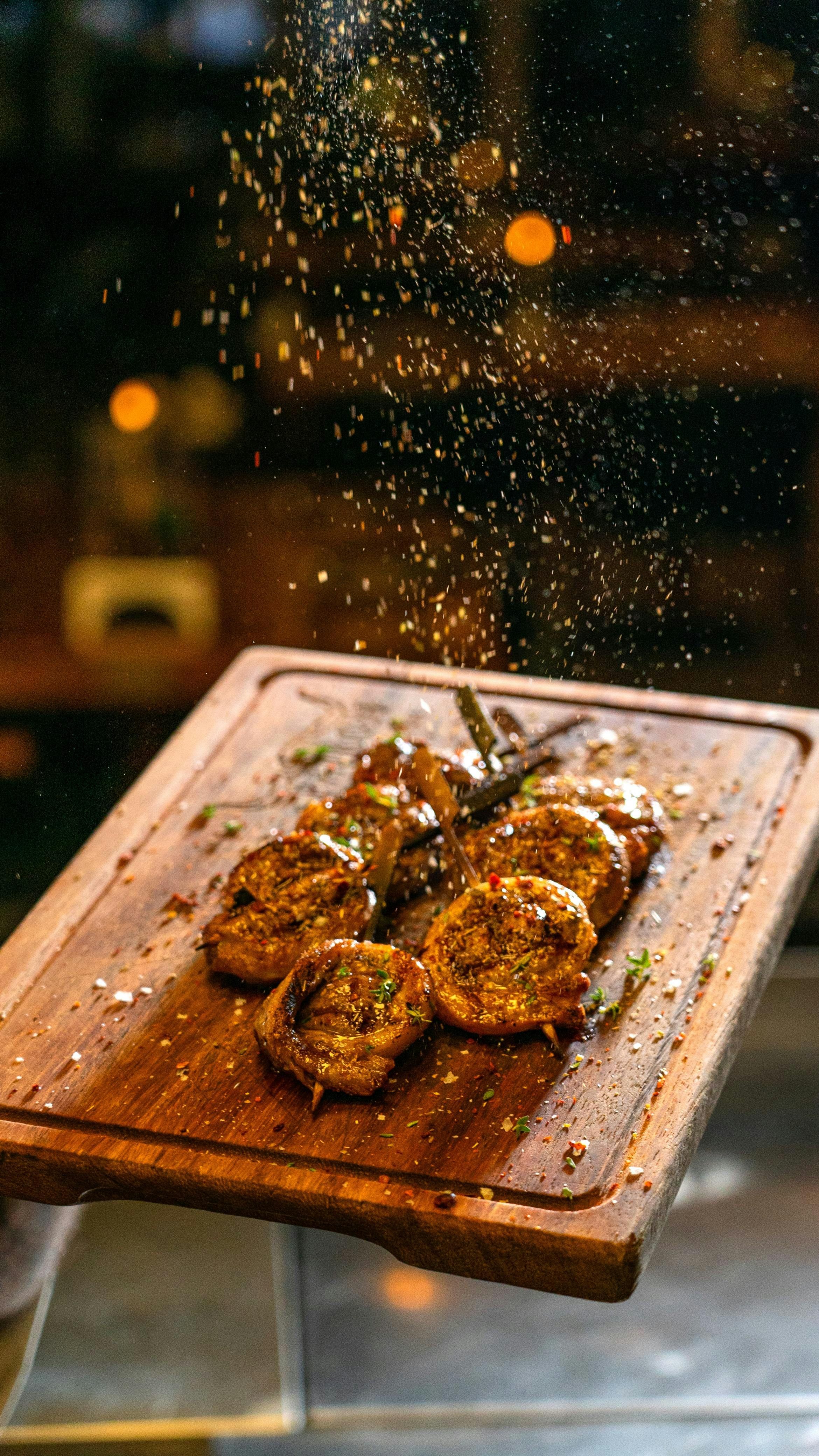 grátis Close-up de carne grelhada temperada em uma travessa de madeira, polvilhada com especiarias. Foto profissional
