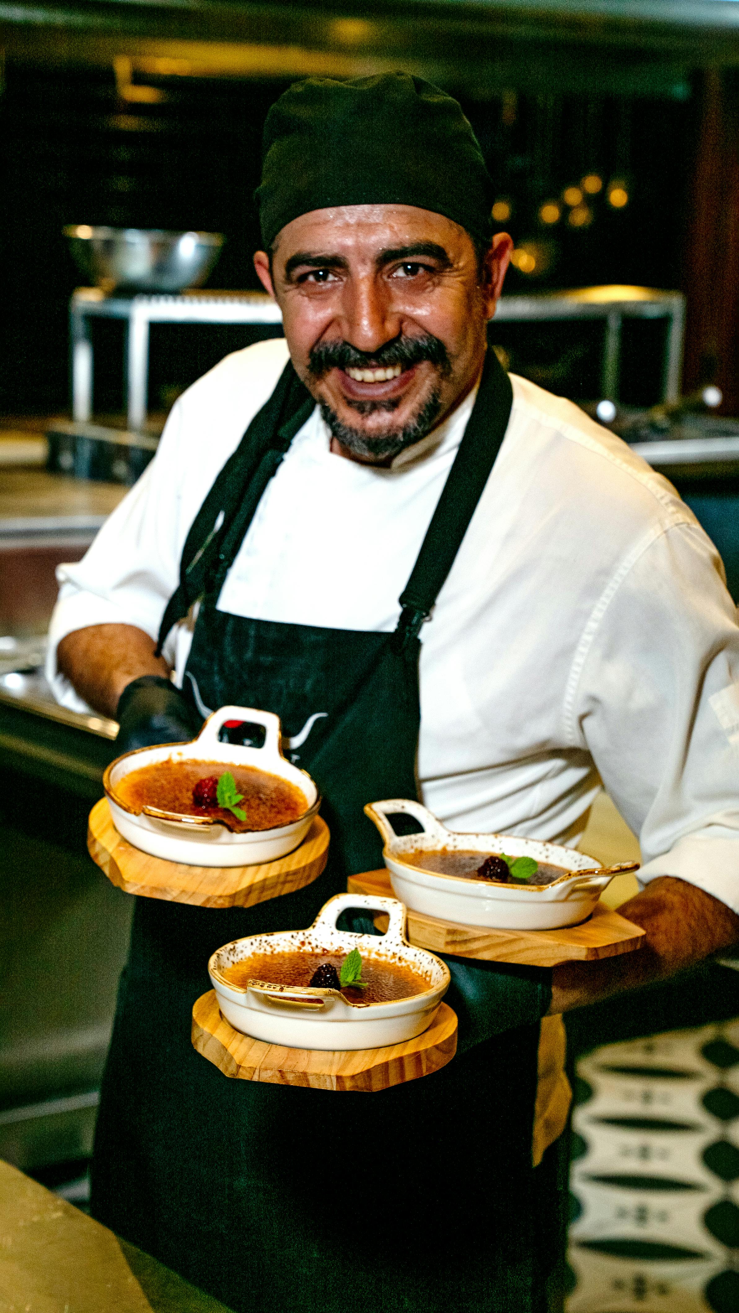 無料 プロの厨房で、シェフが笑顔で美しく盛り付けられた3種類のデザートを披露している。 写真素材