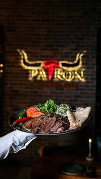 Close-up of a steak dish with salad and flatbread, served in a stylish restaurant.