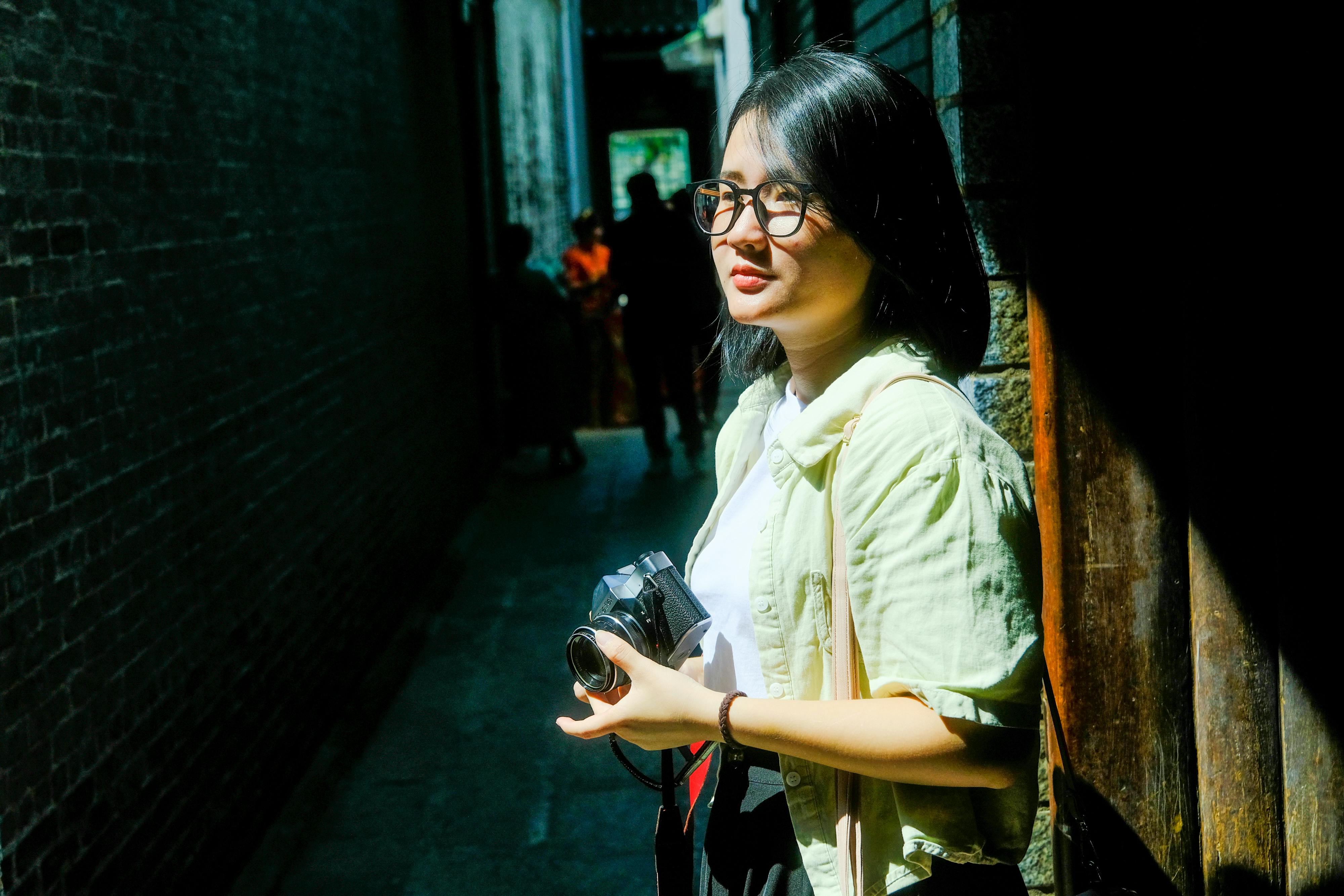 免費 越南順化一條陽光明媚的小巷裡，一位年輕女子手持攝影機。 圖庫相片