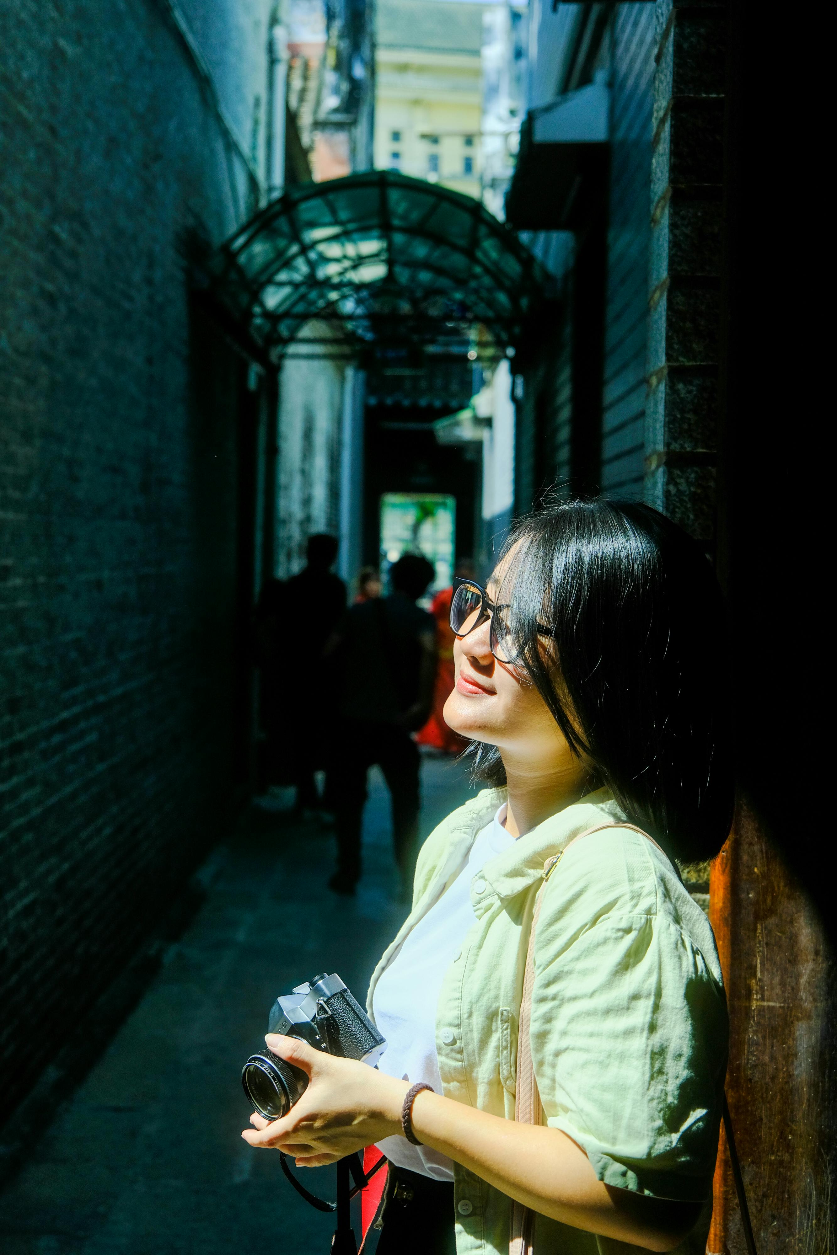 Безкоштовне Жінка насолоджується сонячним світлом на жвавій алеї міста Хюе, фіксуючи моменти на камеру. стокове фото