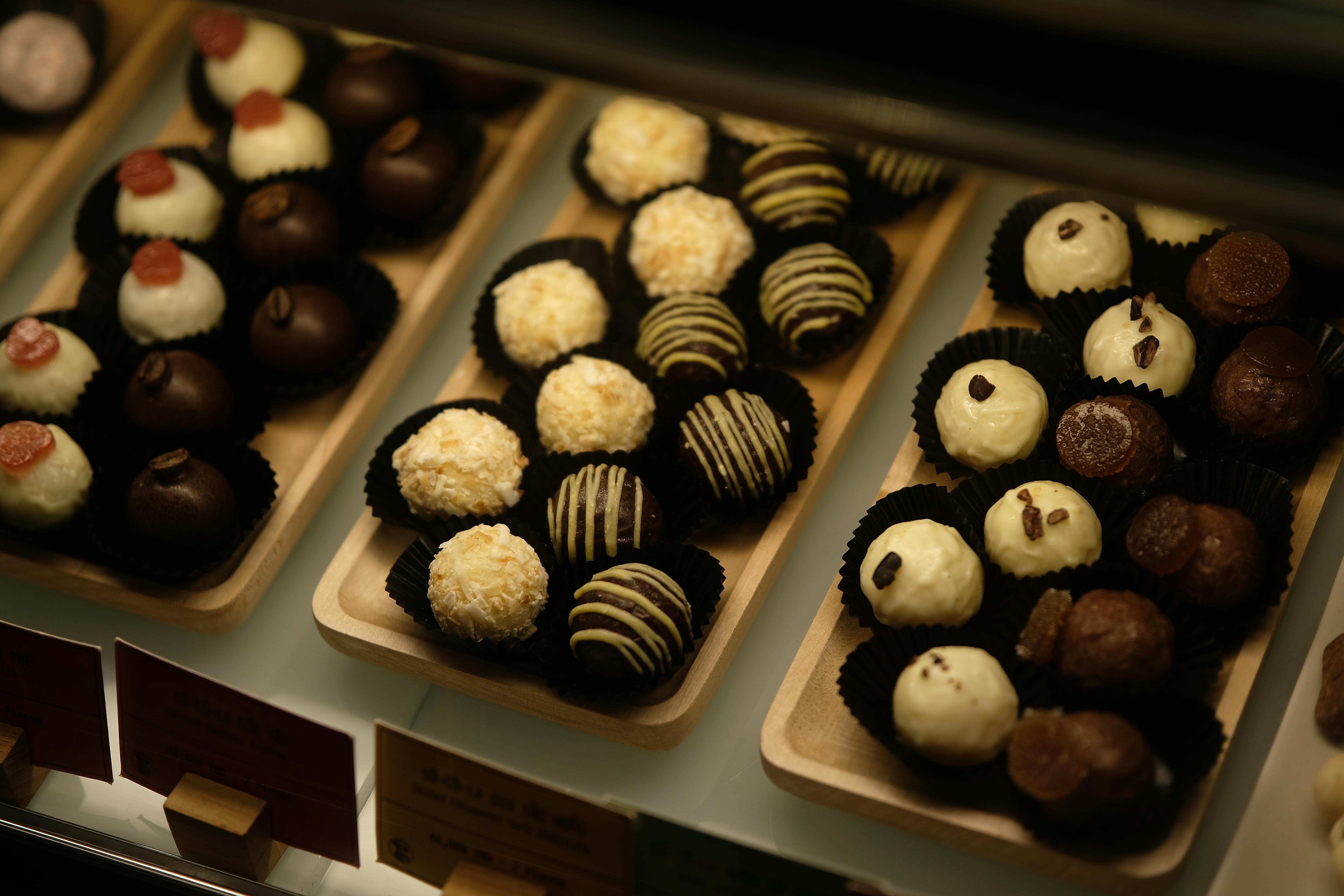 Gratuit Un assortiment appétissant de truffes au chocolat variées, présentées sur des plateaux en bois sous un éclairage chaleureux. Photos