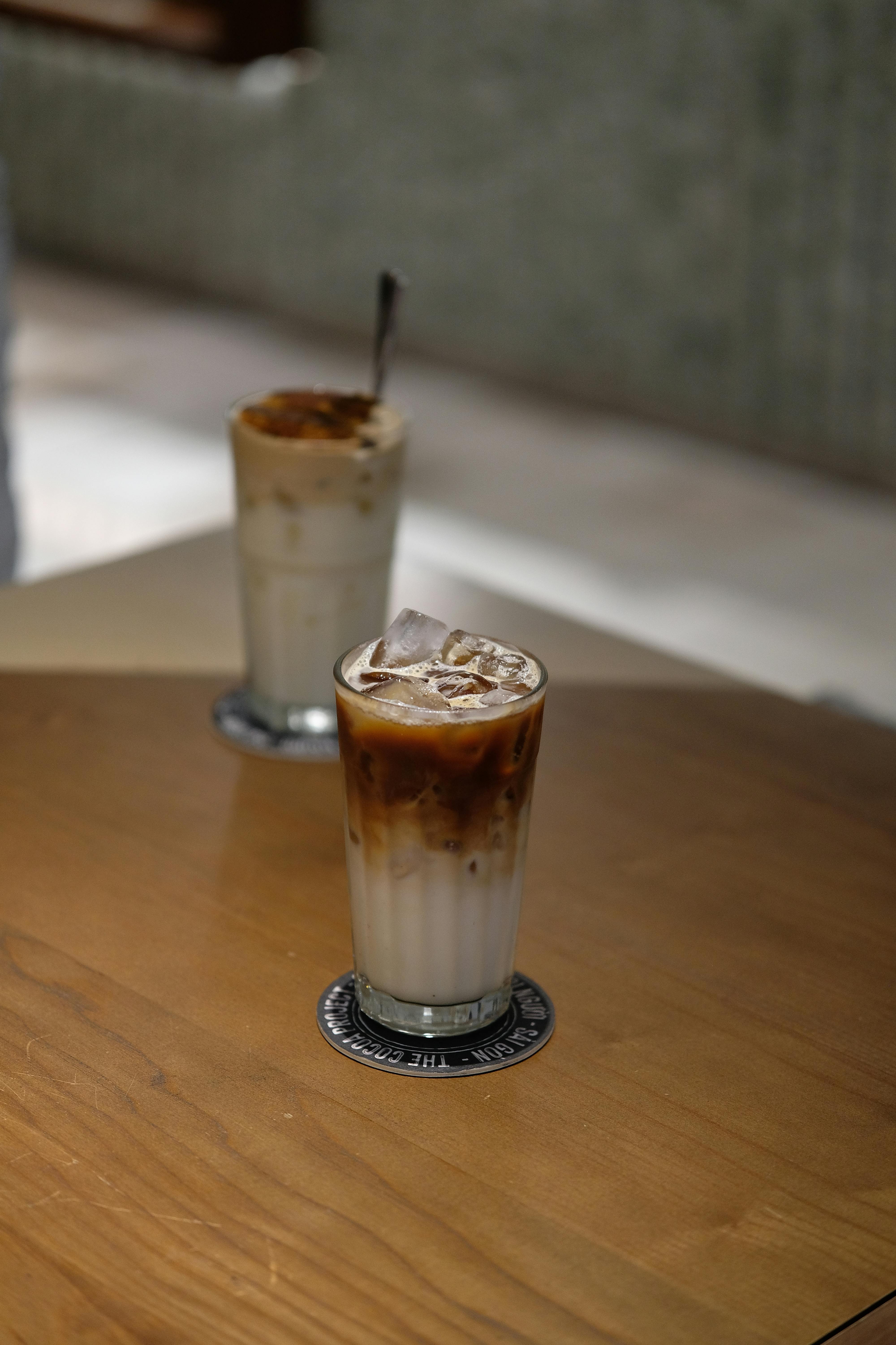 無料 室内で撮影されたアイスラテのクローズアップ写真。もう1つの飲み物はぼやけて写っている。 写真素材