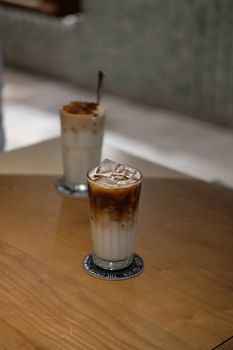 Close-up of iced latte with a second blurred drink in an indoor setting.