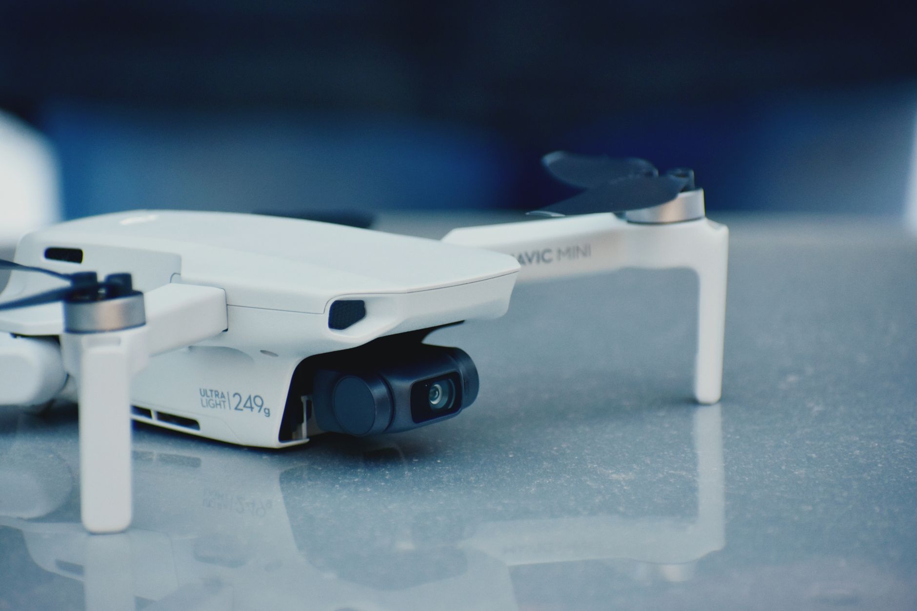 Close-up of a white drone on a reflective surface, showcasing its camera and sleek design.