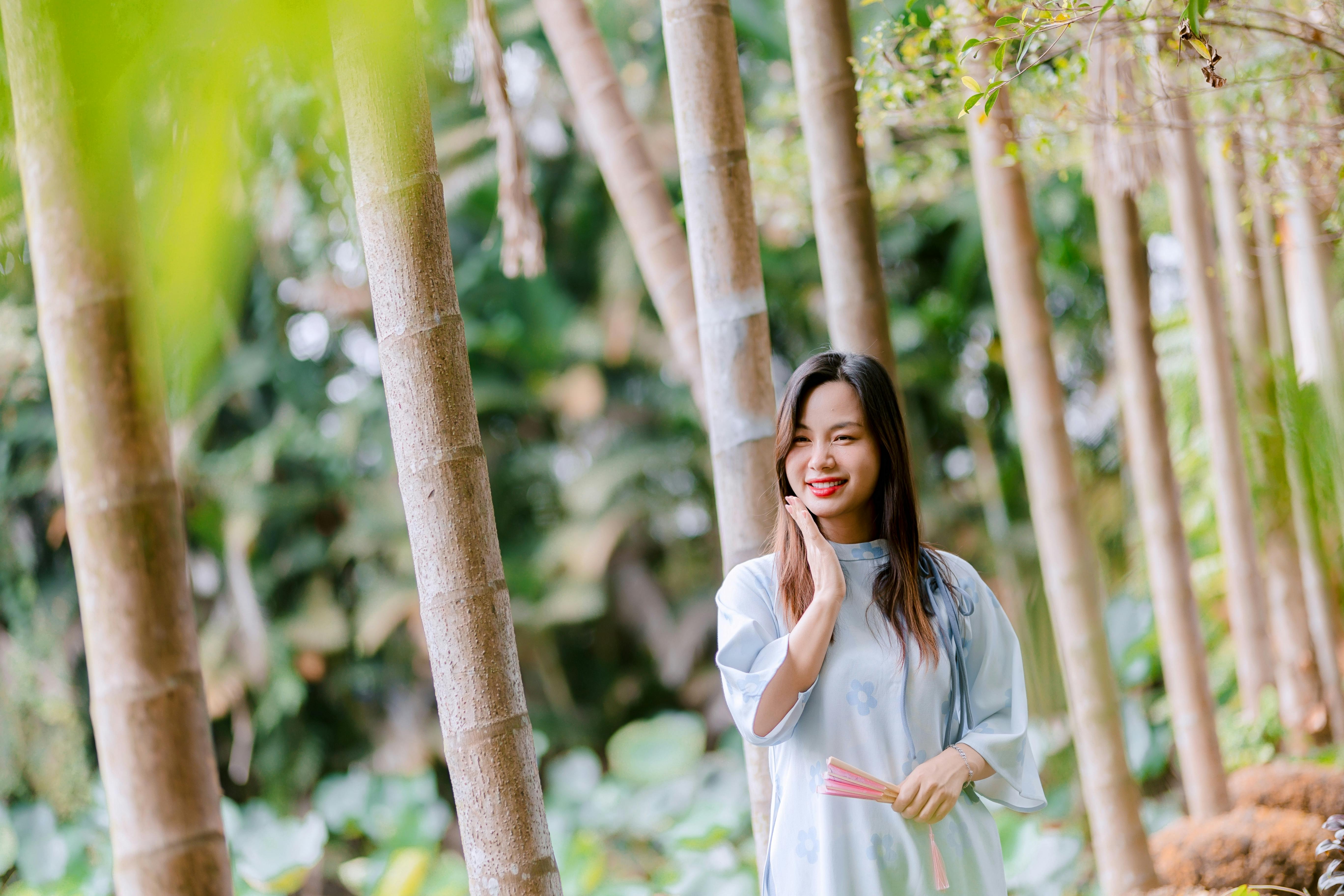 Bezpłatne Uśmiechnięta młoda kobieta w spokojnym otoczeniu bambusowego gaju, ciesząca się naturą. Zdjęcie z galerii