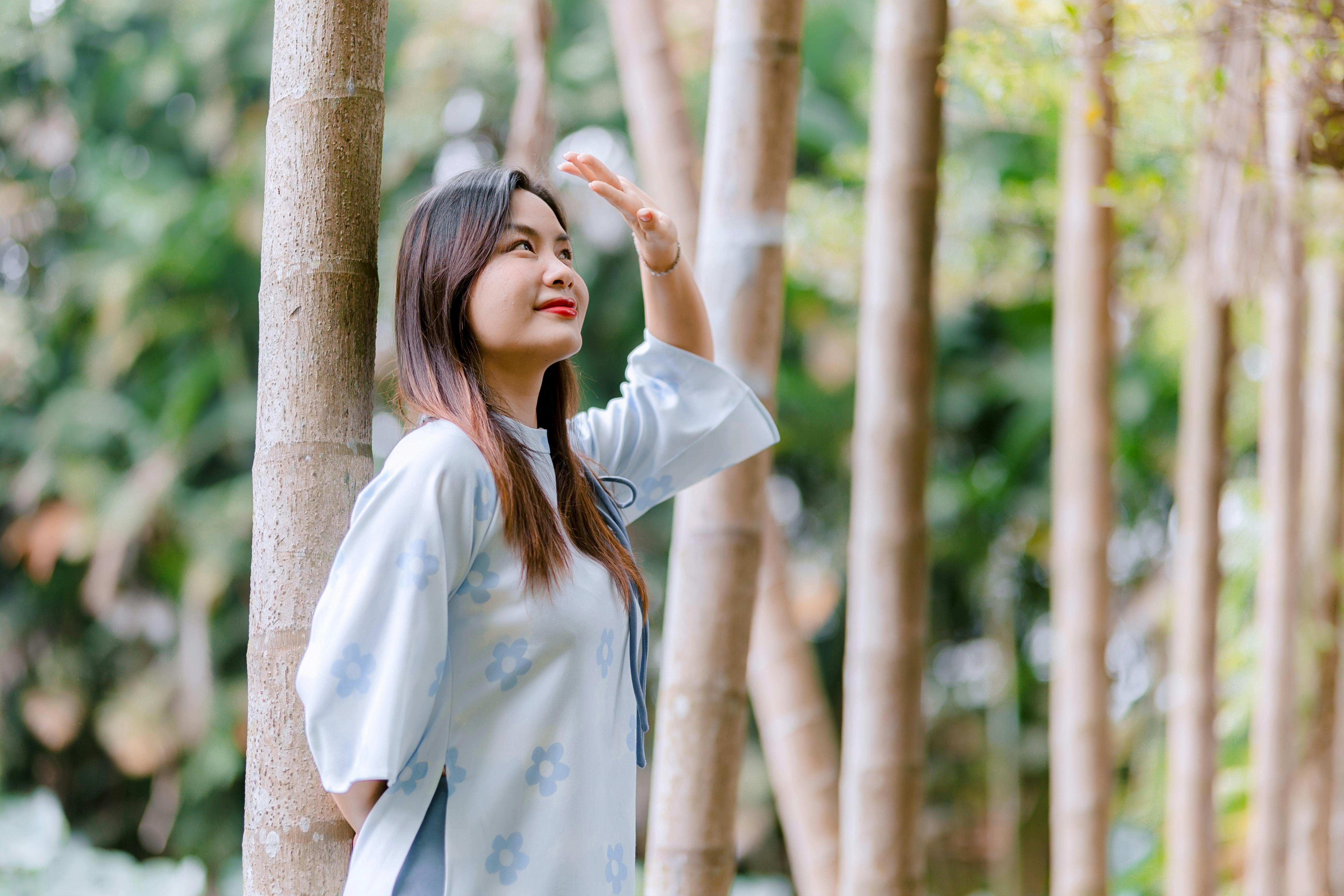 Gratis Mujer sonriente con vestido blanco disfrutando de un día soleado entre árboles altos al aire libre. Foto de stock