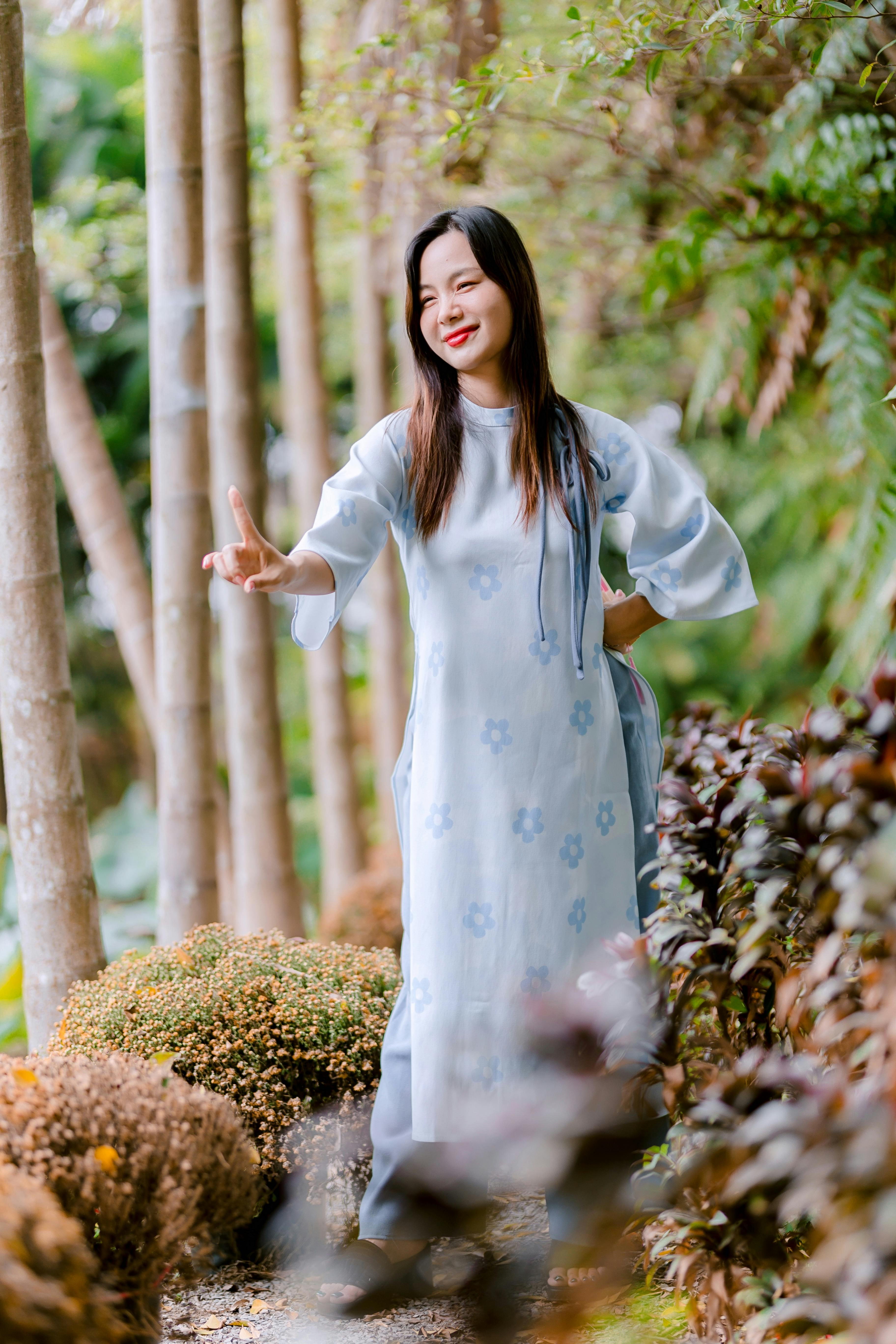 Bezpłatne Kobieta ubrana w kwiecistą sukienkę cieszy się spokojnym spacerem pośród natury, w otoczeniu drzew i zieleni. Zdjęcie z galerii