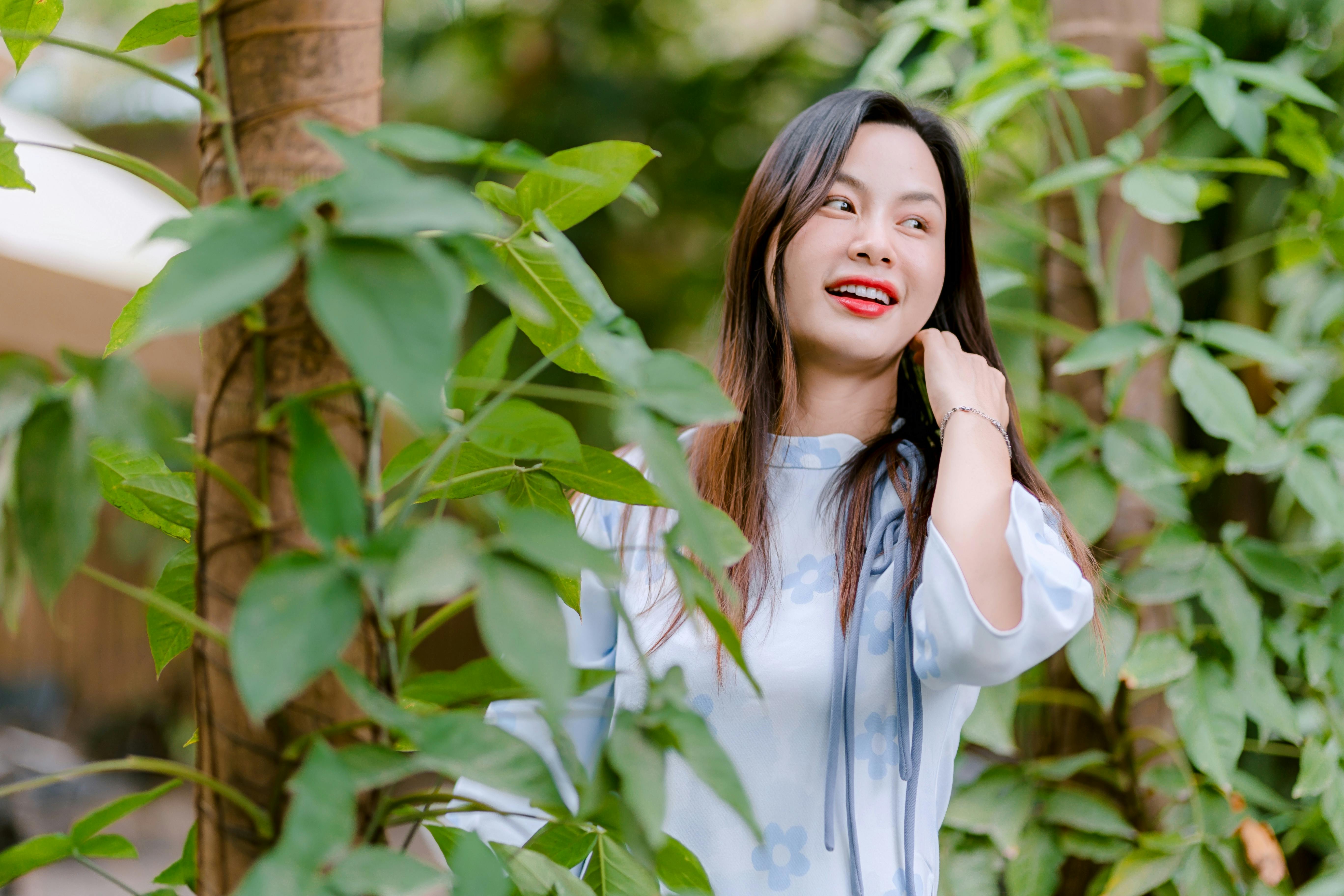 Gratuit Jeune femme rayonnante posant au milieu d'une végétation luxuriante en extérieur, dégageant un bonheur immense. Photos