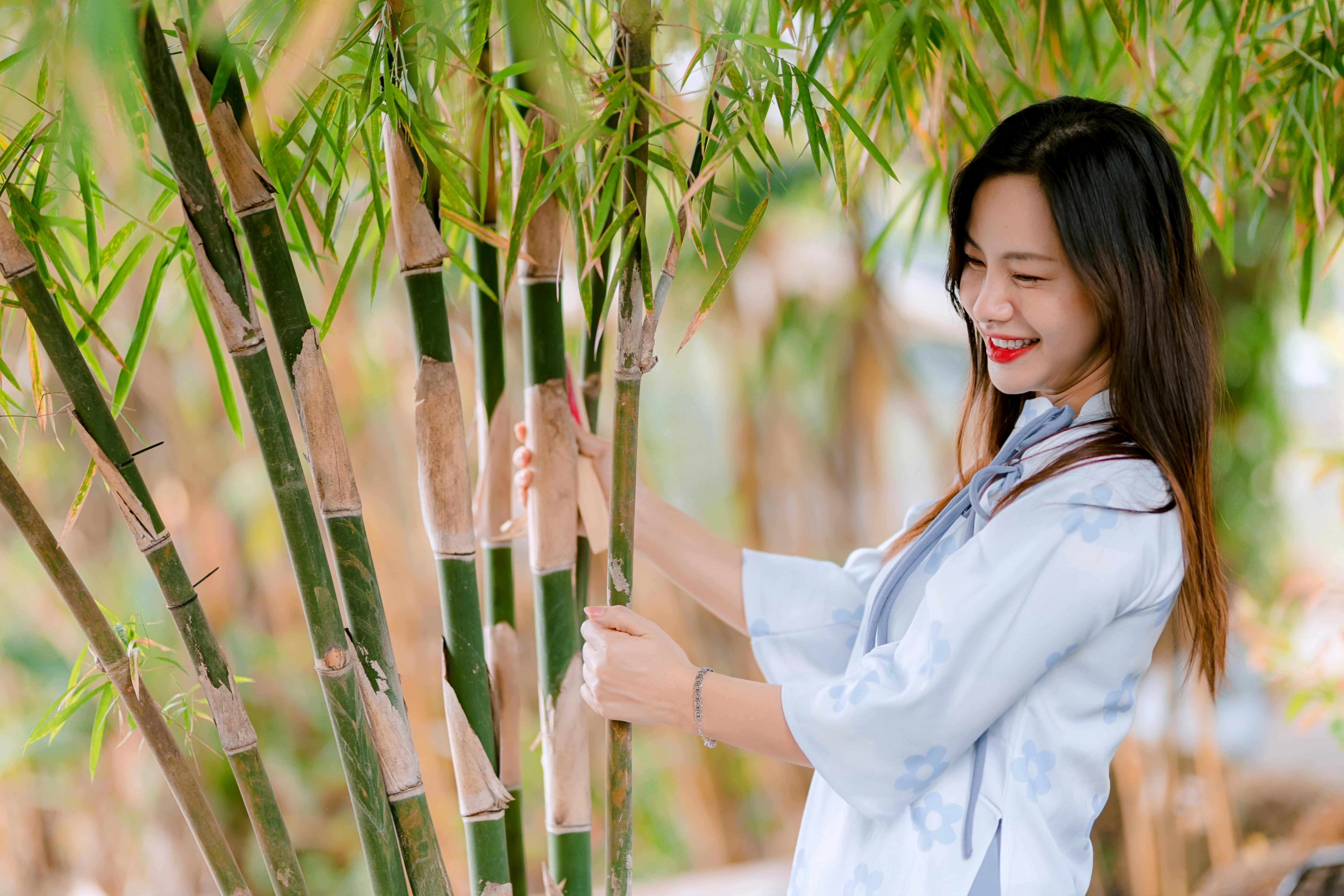 gratis Een vrolijke vrouw in een serene bamboetuin, die rust en positiviteit uitstraalt. Stockfoto