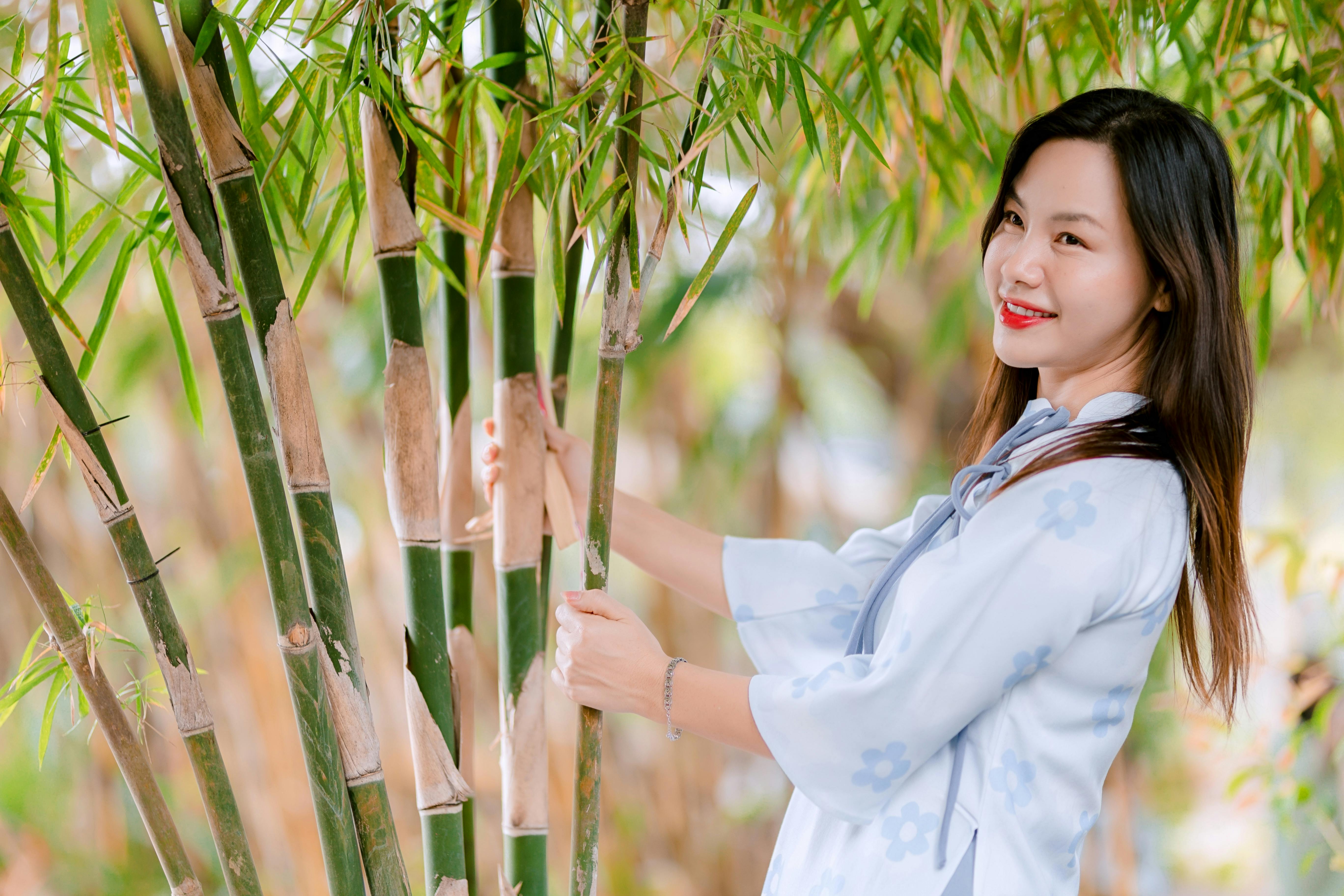Gratis Mujer sonriente con vestido azul disfrutando de la naturaleza rodeada de tallos de bambú. Foto de stock