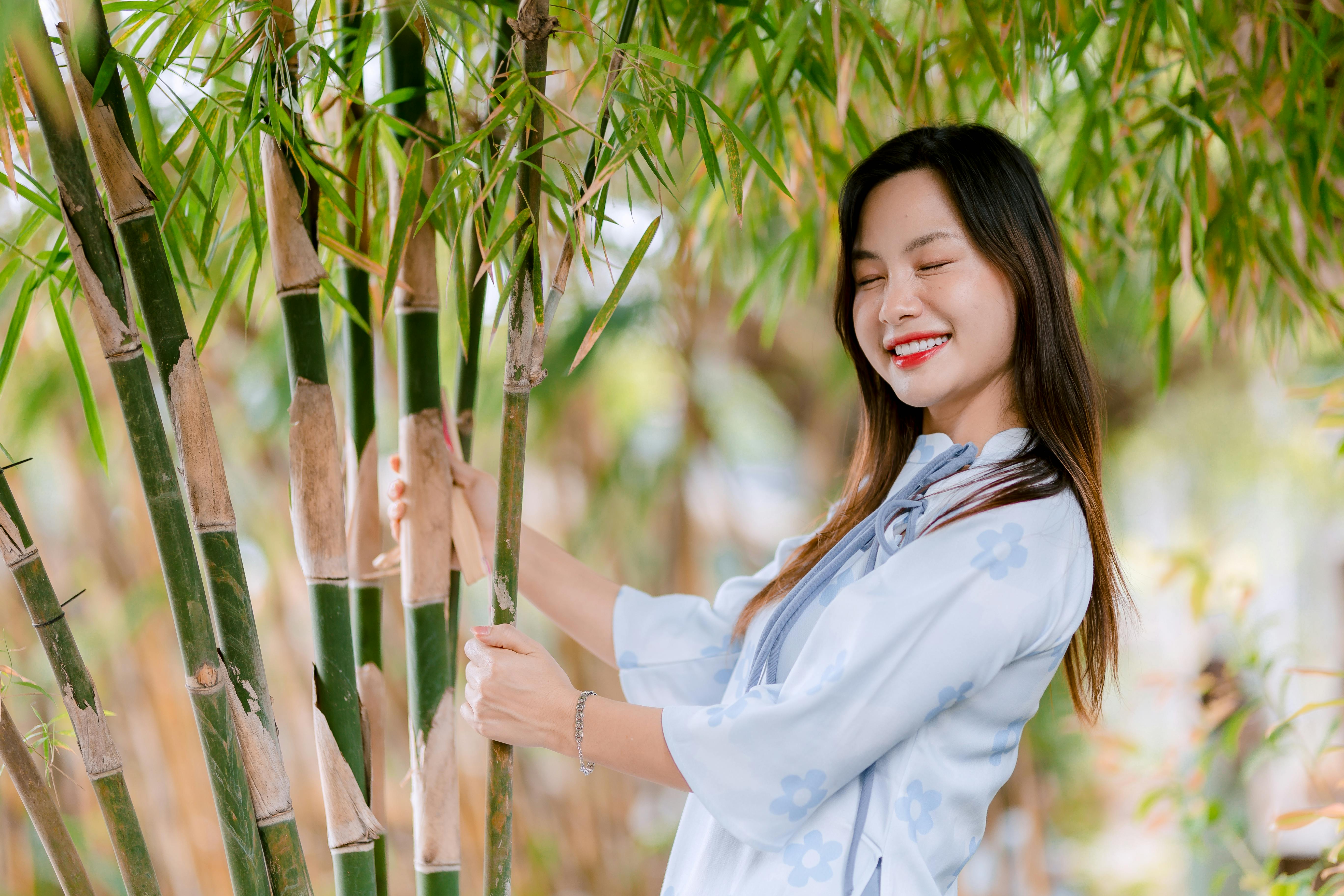 免费 一位身穿浅蓝色连衣裙的快乐女子站在户外竹林中，浑身散发着幸福的气息。 素材图片