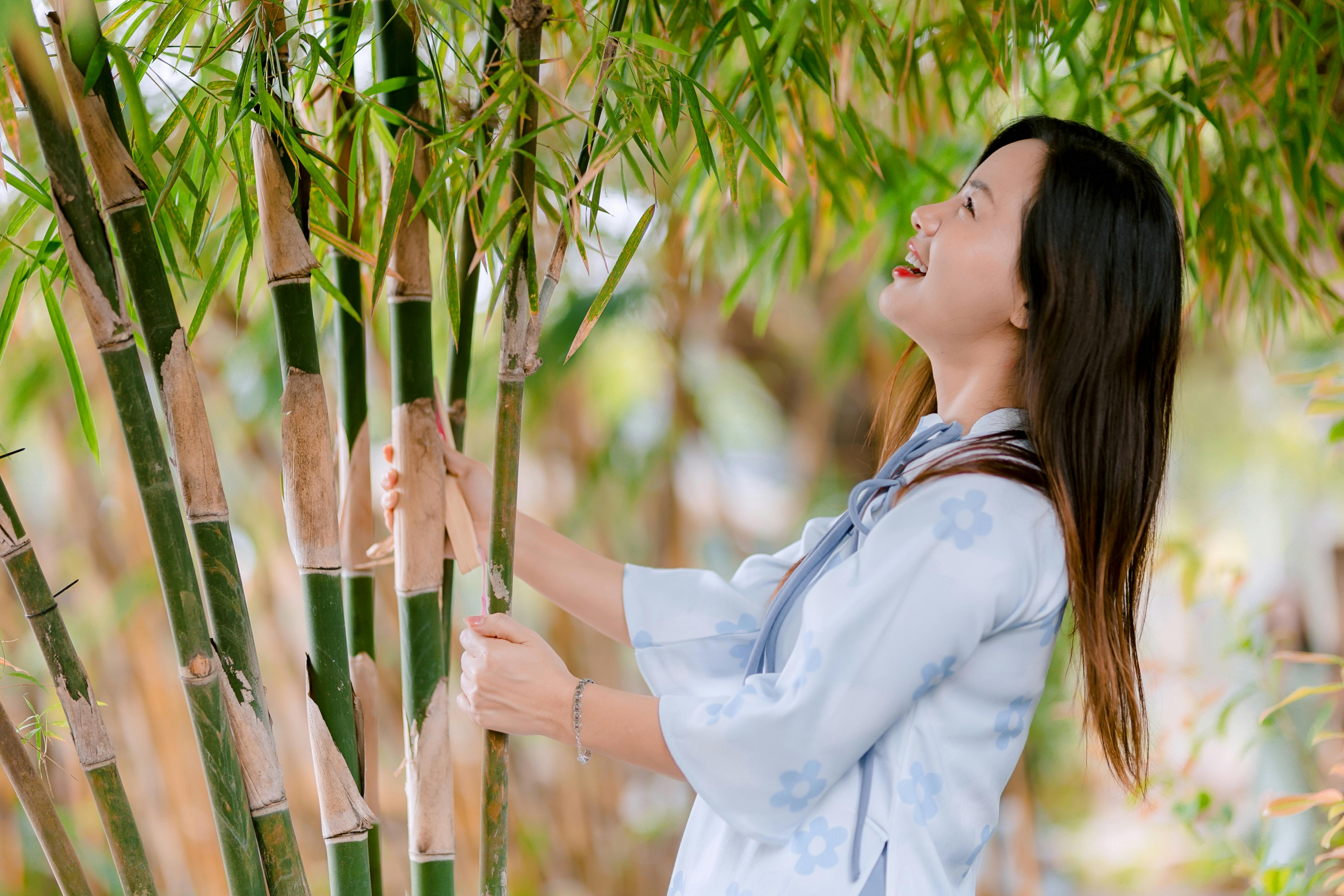 Bezpłatne Uśmiechnięta kobieta w bambusowym gaju cieszy się naturą i spokojem. Zdjęcie z galerii