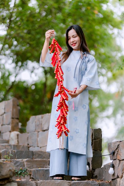 Free Smiling woman in traditional dress celebrating with red firecrackers outdoors against nature backdrop. Stock Photo
