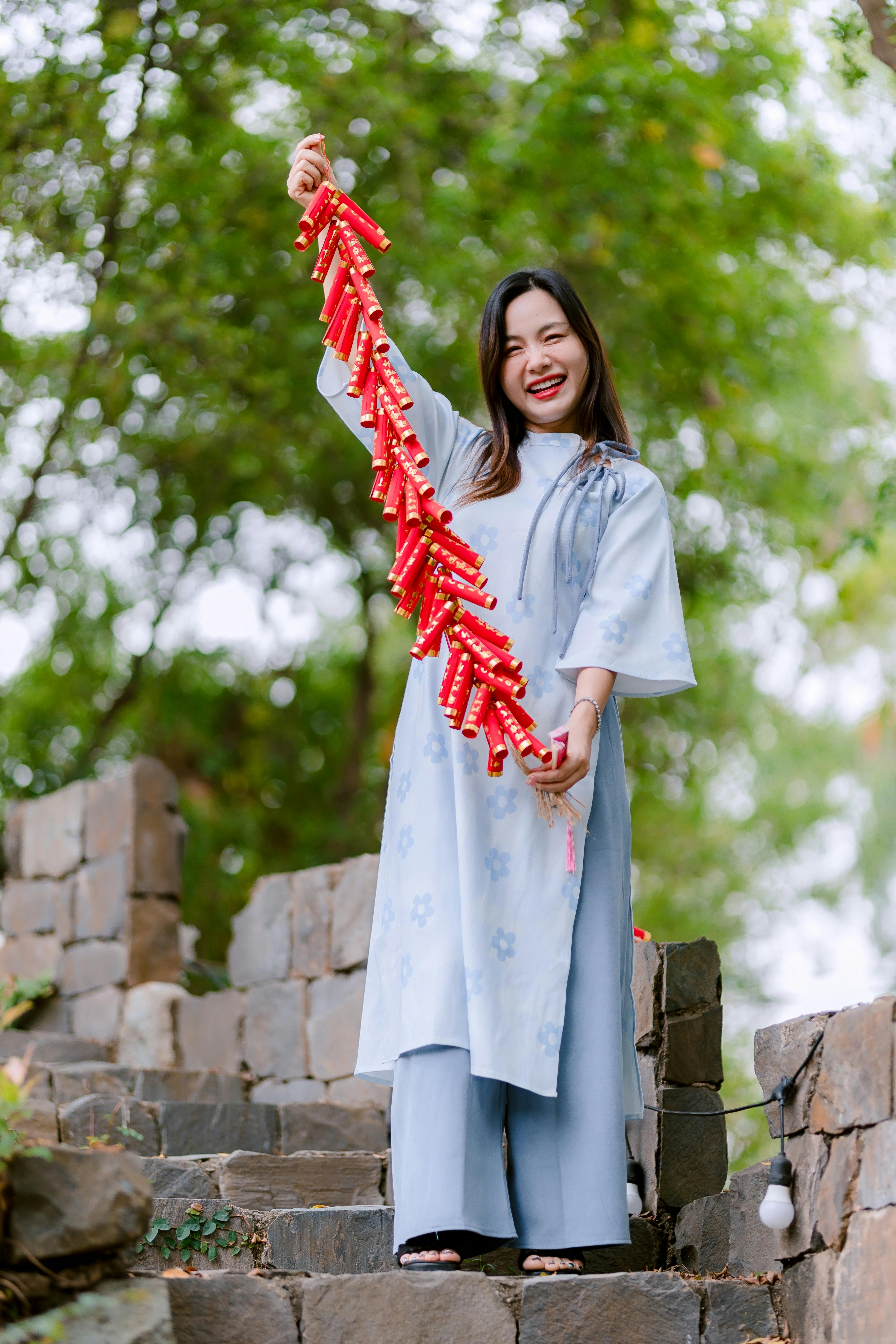 免费 一位面带微笑的女子在户外石阶上手持红色鞭炮，正在庆祝。 素材图片