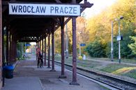A lone bicyclist waits at the Wrocław Pracze train station on a sunny autumn day.