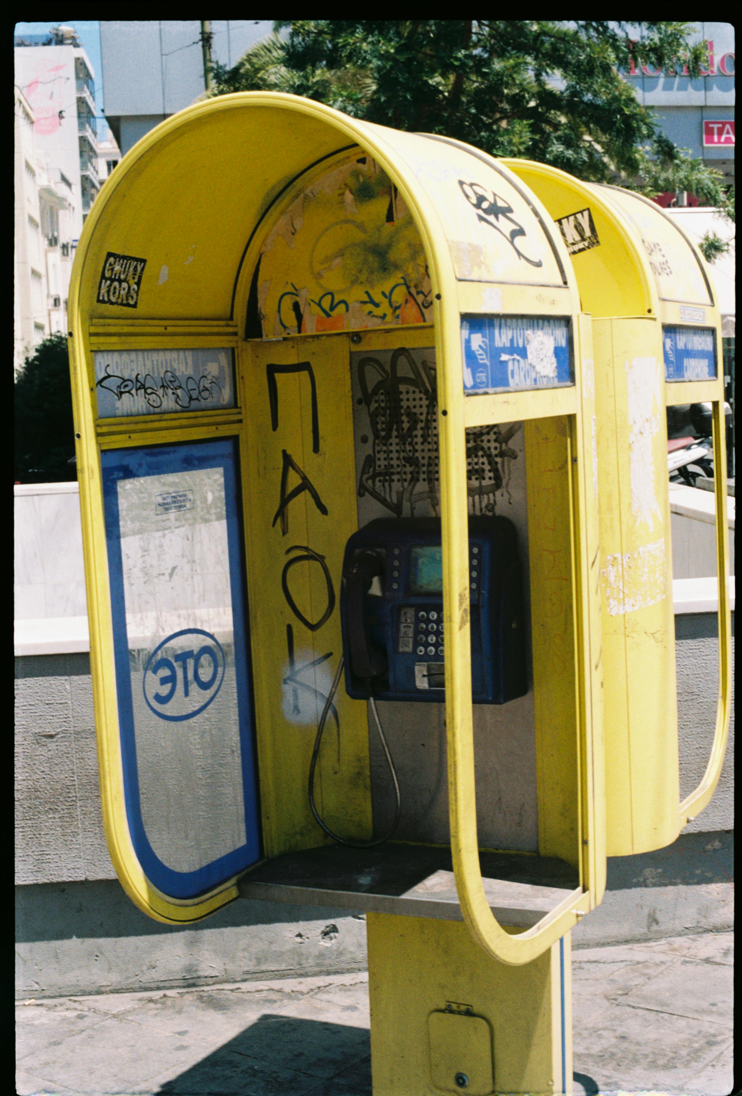 Gratis En forvitret gul telefonboks dækket af graffiti tilføjer bymæssig charme. Lagerfoto