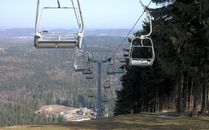 Empty ski lift chairs suspended over a vast forested mountain view, under a clear sky.