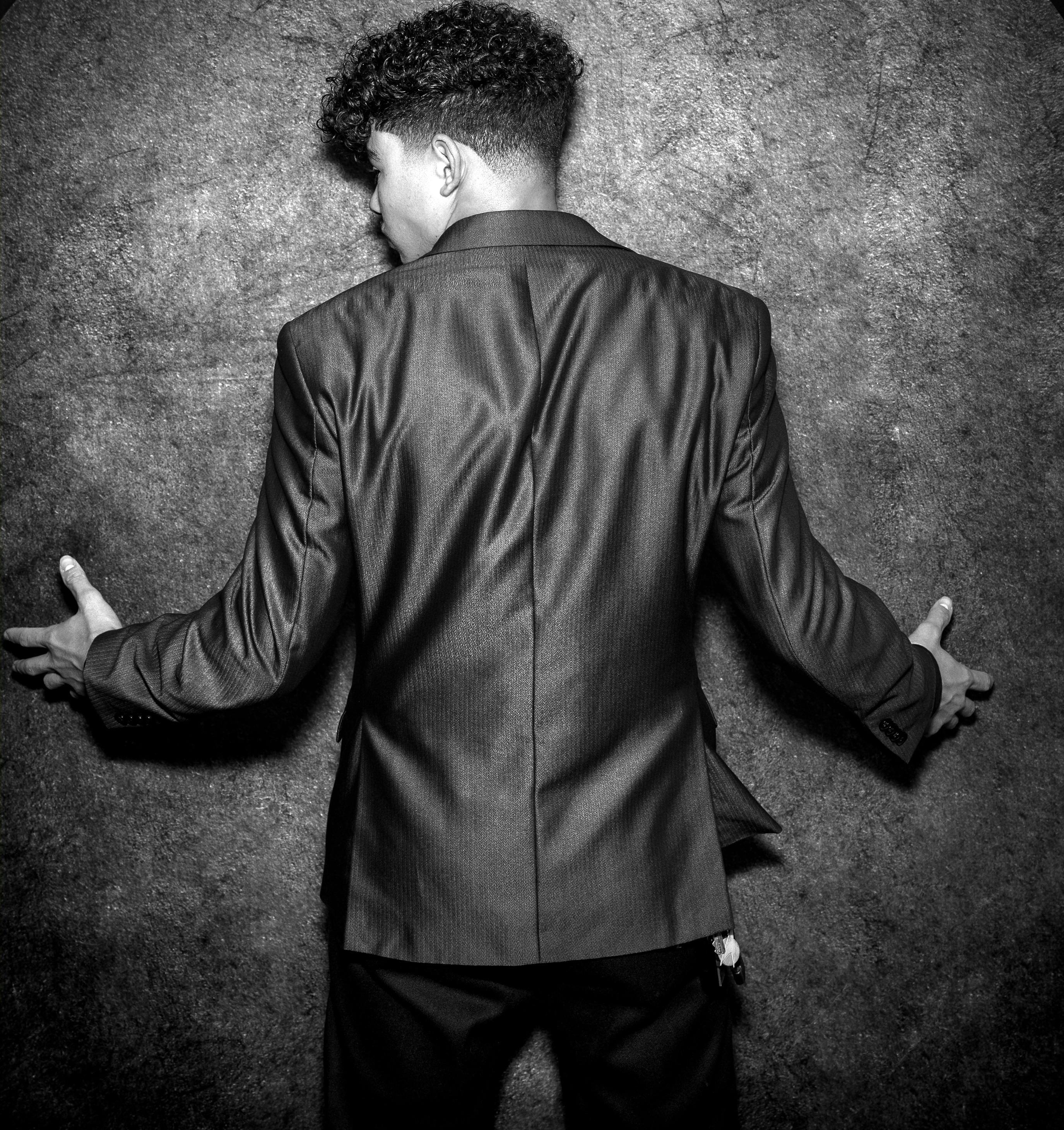 Gratuit Un tânăr într-un costum negru cu fața spre un perete texturat, surprins din spate, în alb și negru. Fotografie de stoc