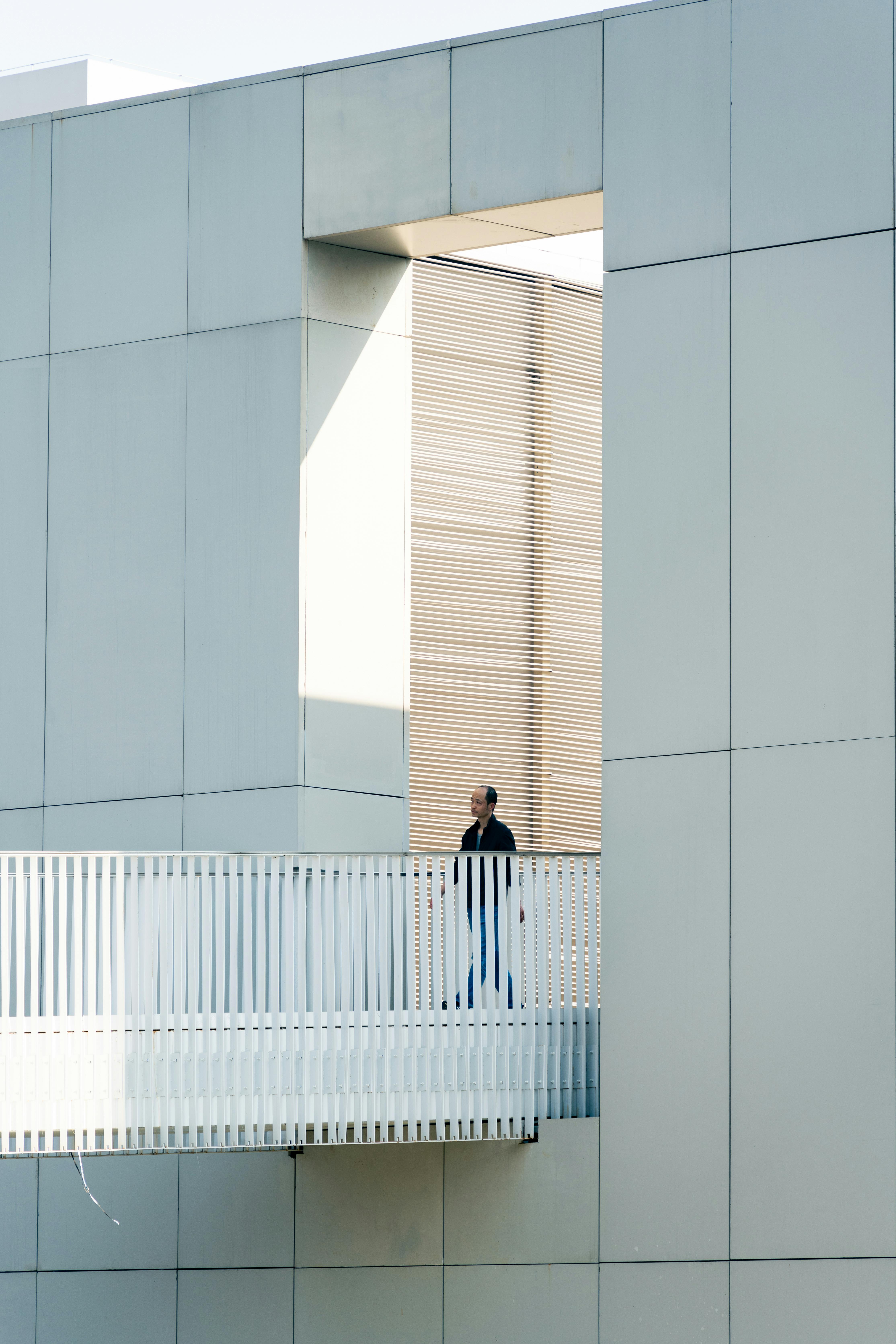 Безкоштовне Чоловік стоїть на балконі на тлі сучасної архітектури з чистими лініями та мінімалістичним дизайном. стокове фото