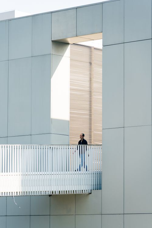 Free A man stands on a balcony against a backdrop of modern architecture with clean lines and minimal design. Stock Photo