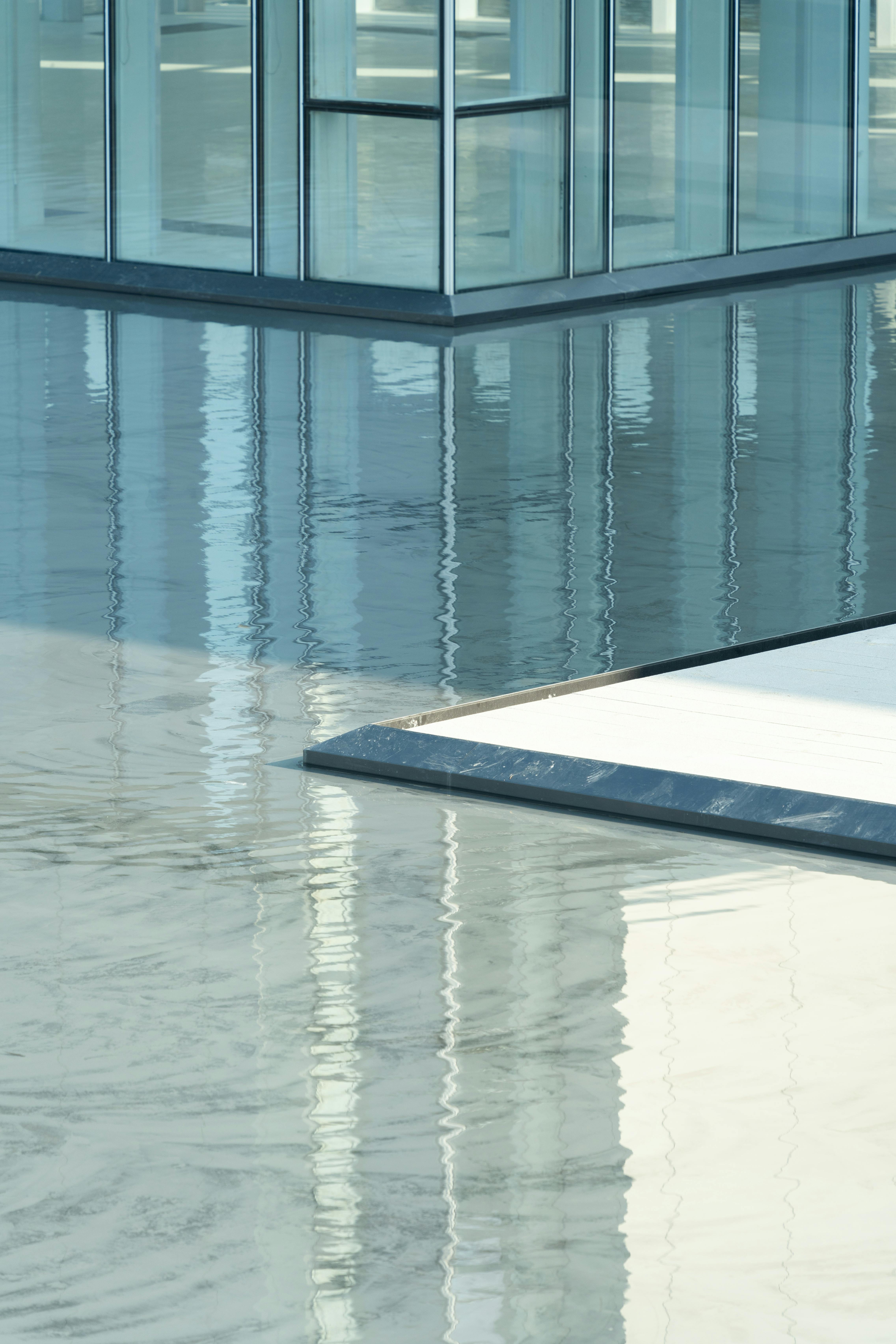 bezplatná Abstraktní pohled na moderní skleněnou budovu odrážející se v klidné vodní hladině, která prezentuje architektonickou eleganci. Základová fotografie