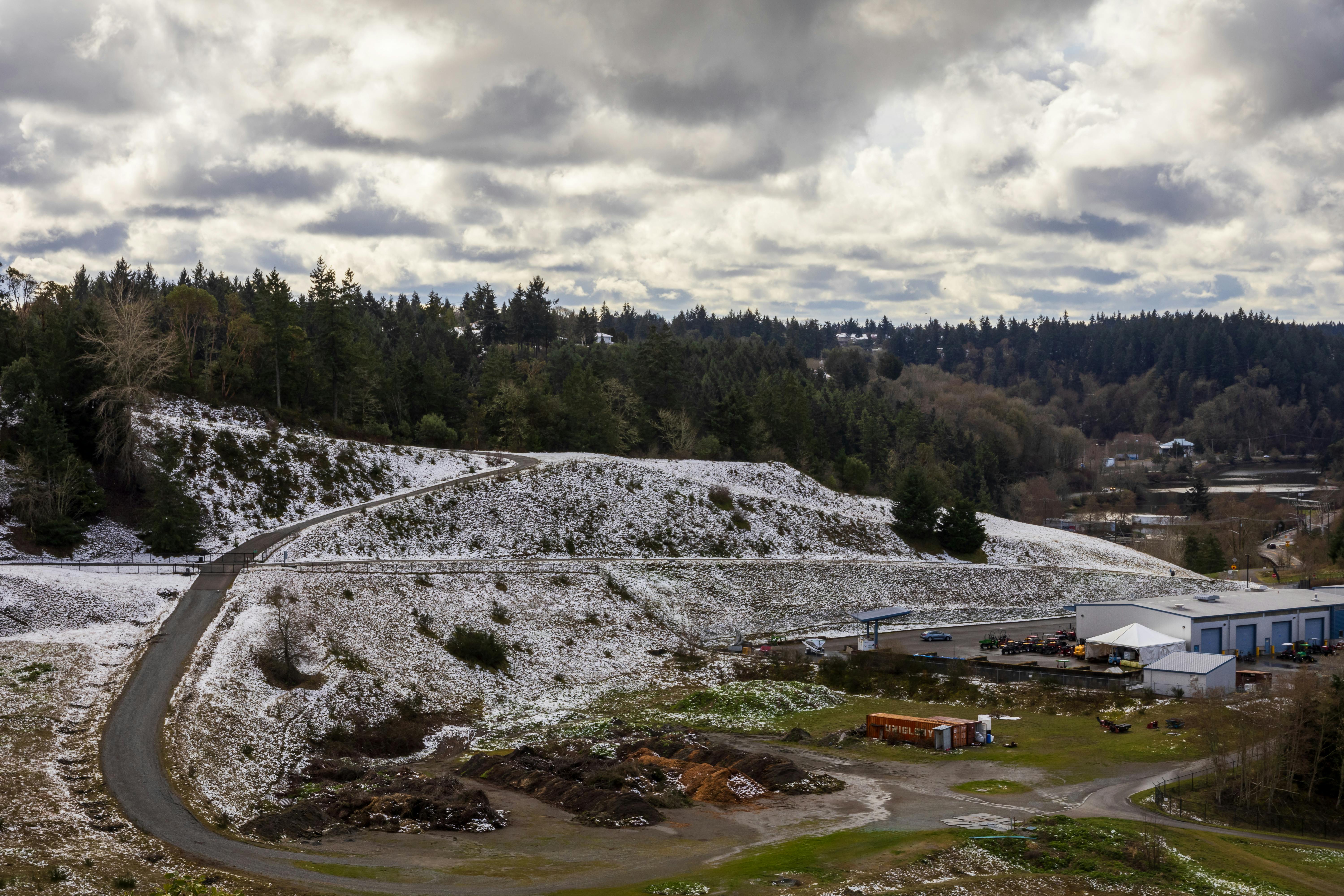 Gratuit Vue pittoresque d'un paysage enneigé, avec une route serpentant à travers une zone industrielle sous un ciel nuageux. Photos