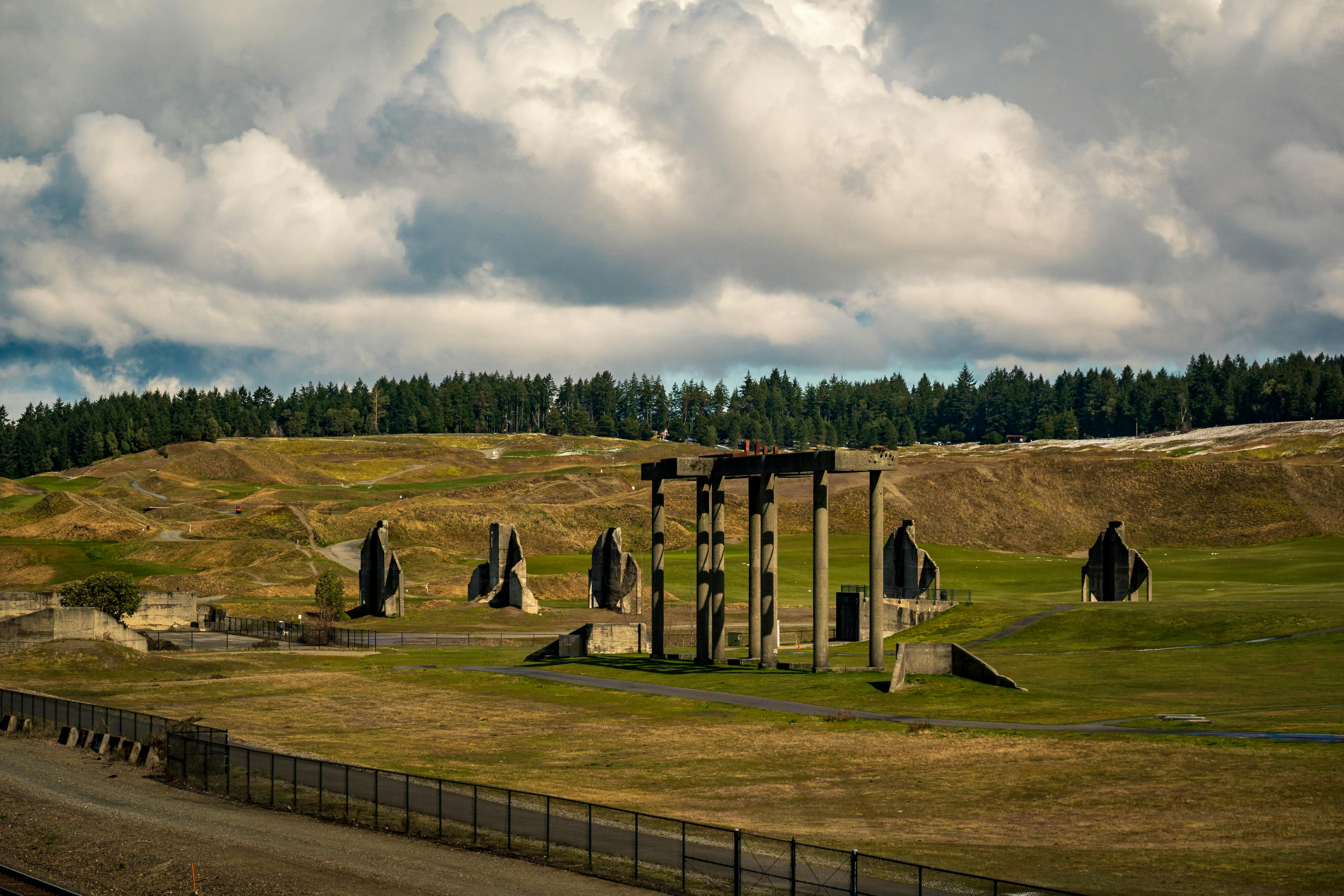 Bezpłatne Dramatyczny krajobraz z betonowymi konstrukcjami wśród pagórków pod zachmurzonym niebem. Zdjęcie z galerii