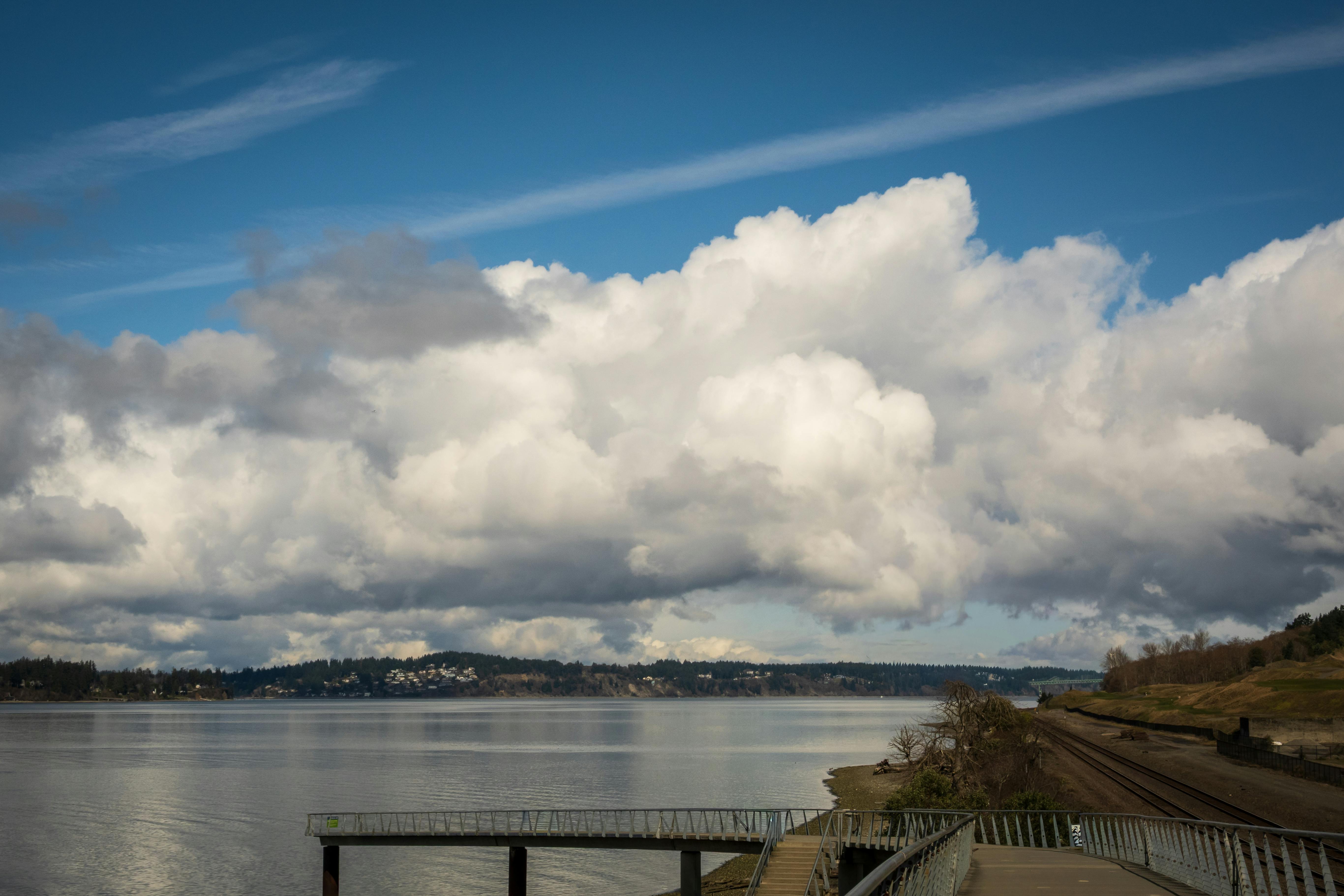 Gratis Fredelig havnefront med dramatiske skyer og fjerne åser under en lys blå himmel. Arkivbilde