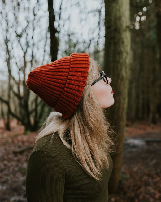 A woman in a red beanie looks up in a forest during autumn. Perfect for seasonal lifestyle concepts.