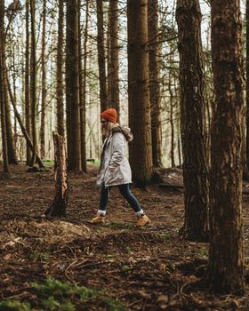 A woman walking in a peaceful wooded area, wearing a beanie and jacket, enjoying nature.