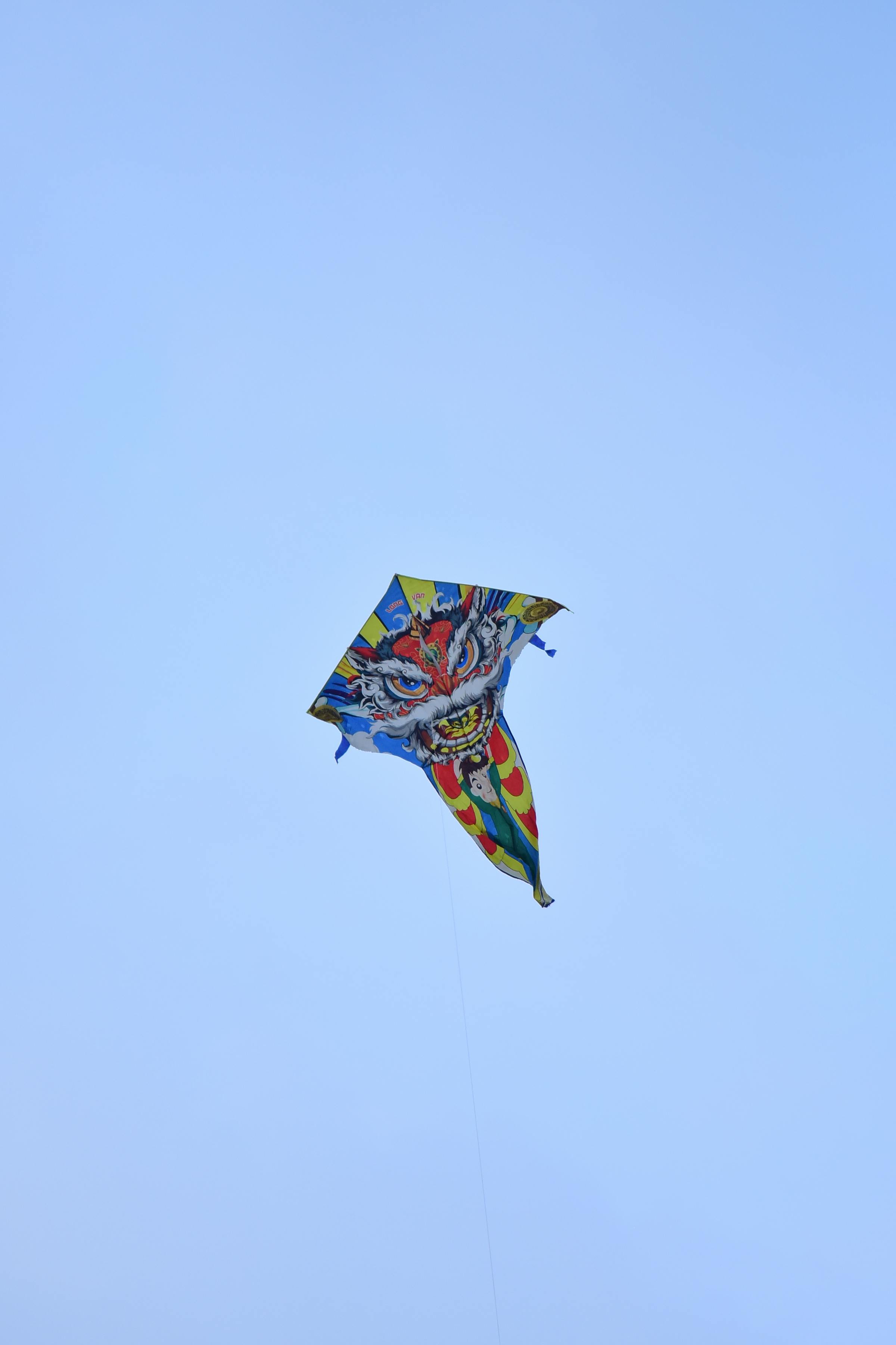 Bezpłatne Jaskrawy latawiec z motywem smoka, unoszący się wysoko na bezchmurnym niebie w pogodny dzień, symbolizujący radość i wolność. Zdjęcie z galerii