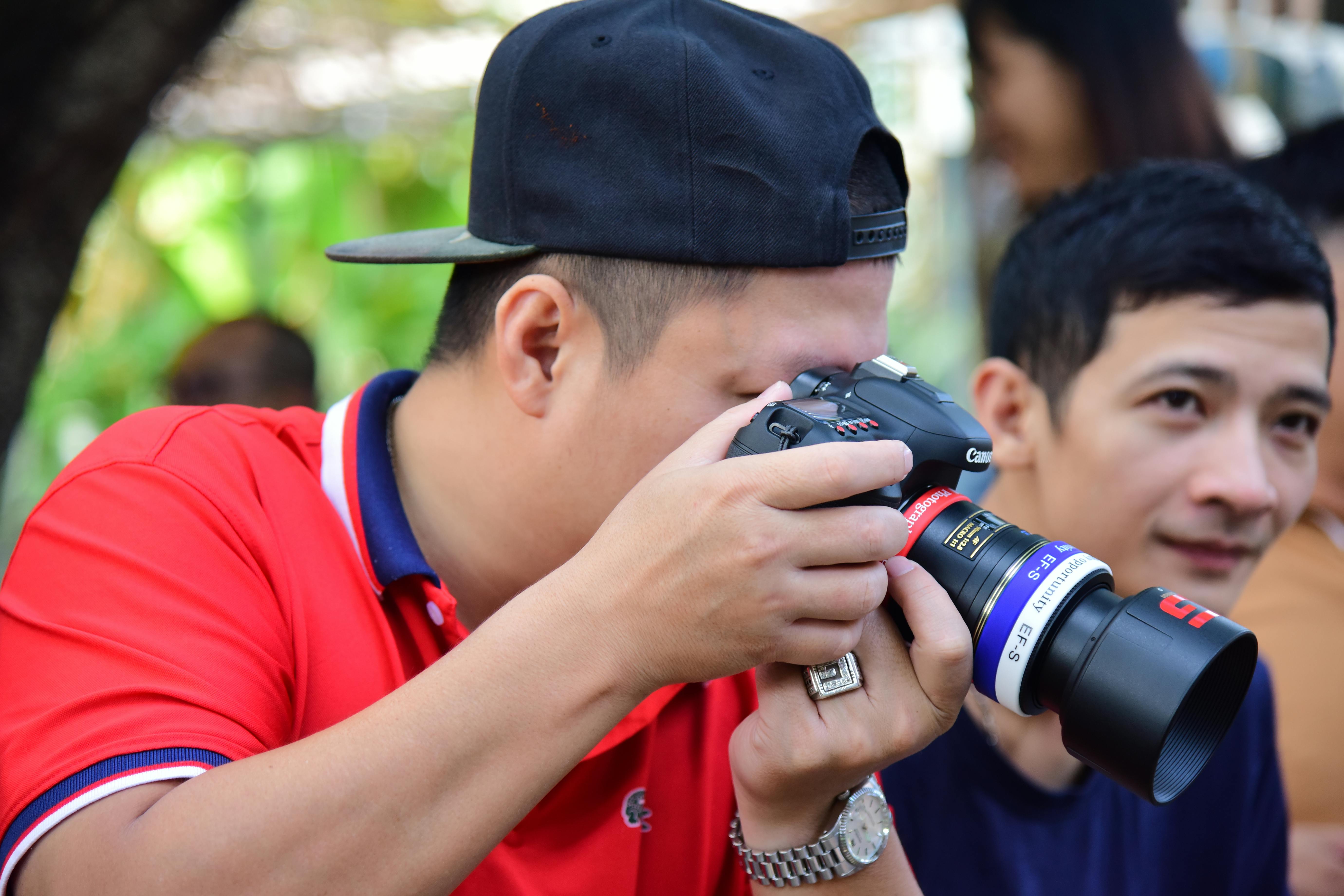 Gratis Un fotógrafo con camisa roja se concentra intensamente mientras captura un momento con una cámara réflex digital al aire libre. Foto de stock