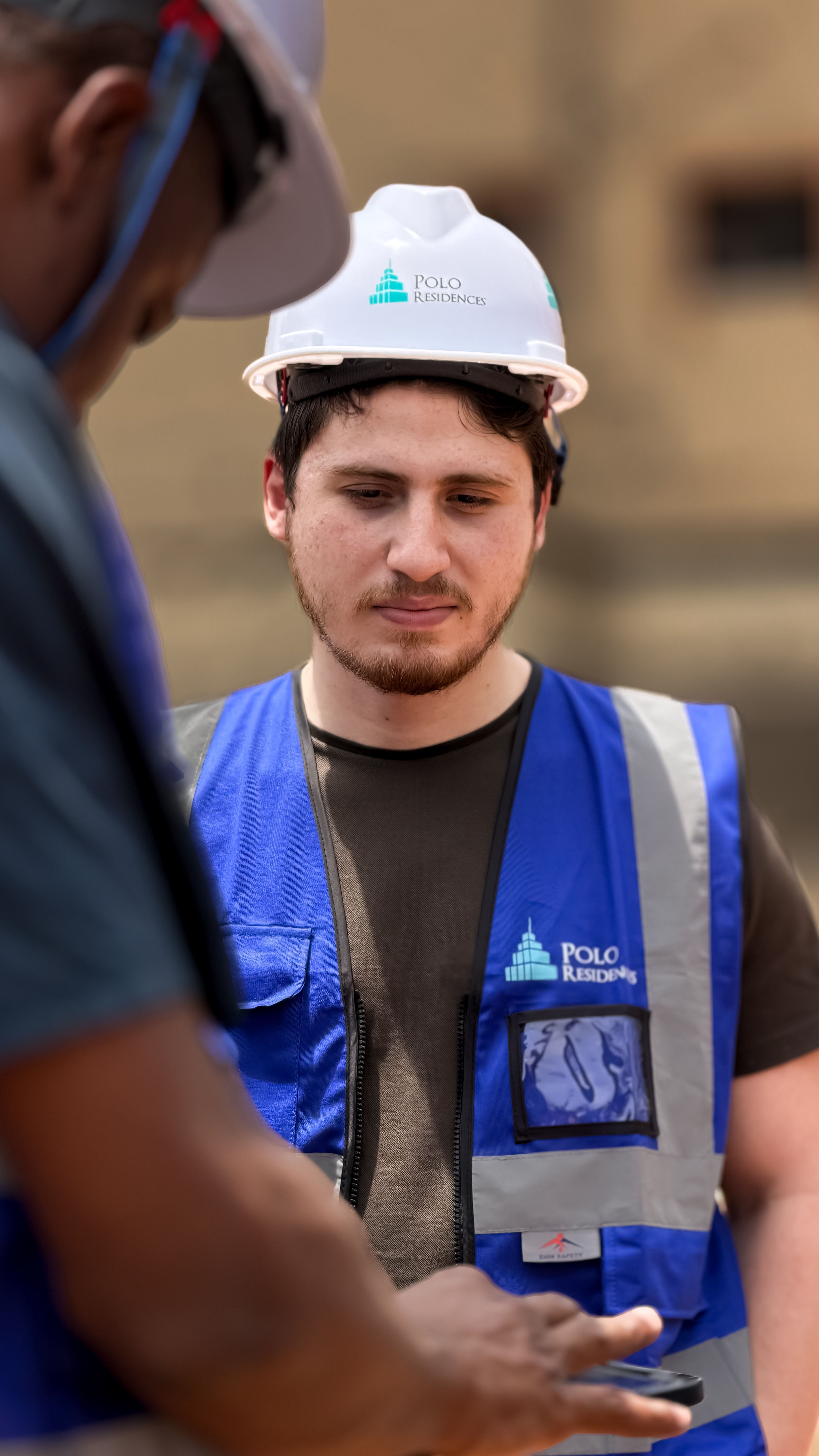 Construction workers engage in discussion outdoors wearing protective gear and blue vests.
