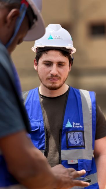 Construction workers engage in discussion outdoors wearing protective gear and blue vests. Construction workers engage in discussion outdoors wearing protective gear and blue vests.
