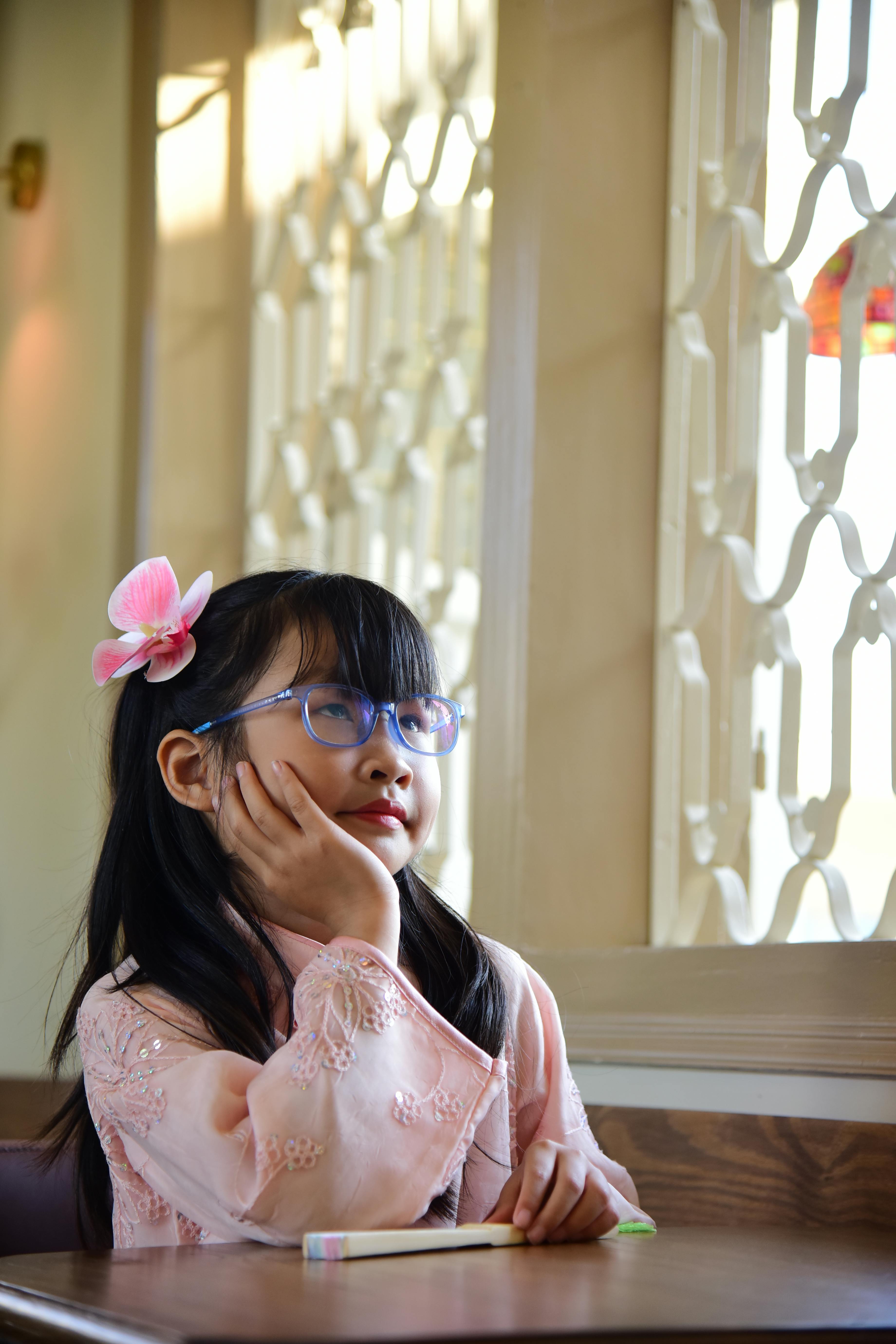 grátis Uma jovem vestida com trajes tradicionais sonha acordada junto a uma janela banhada por uma suave luz natural. Foto profissional