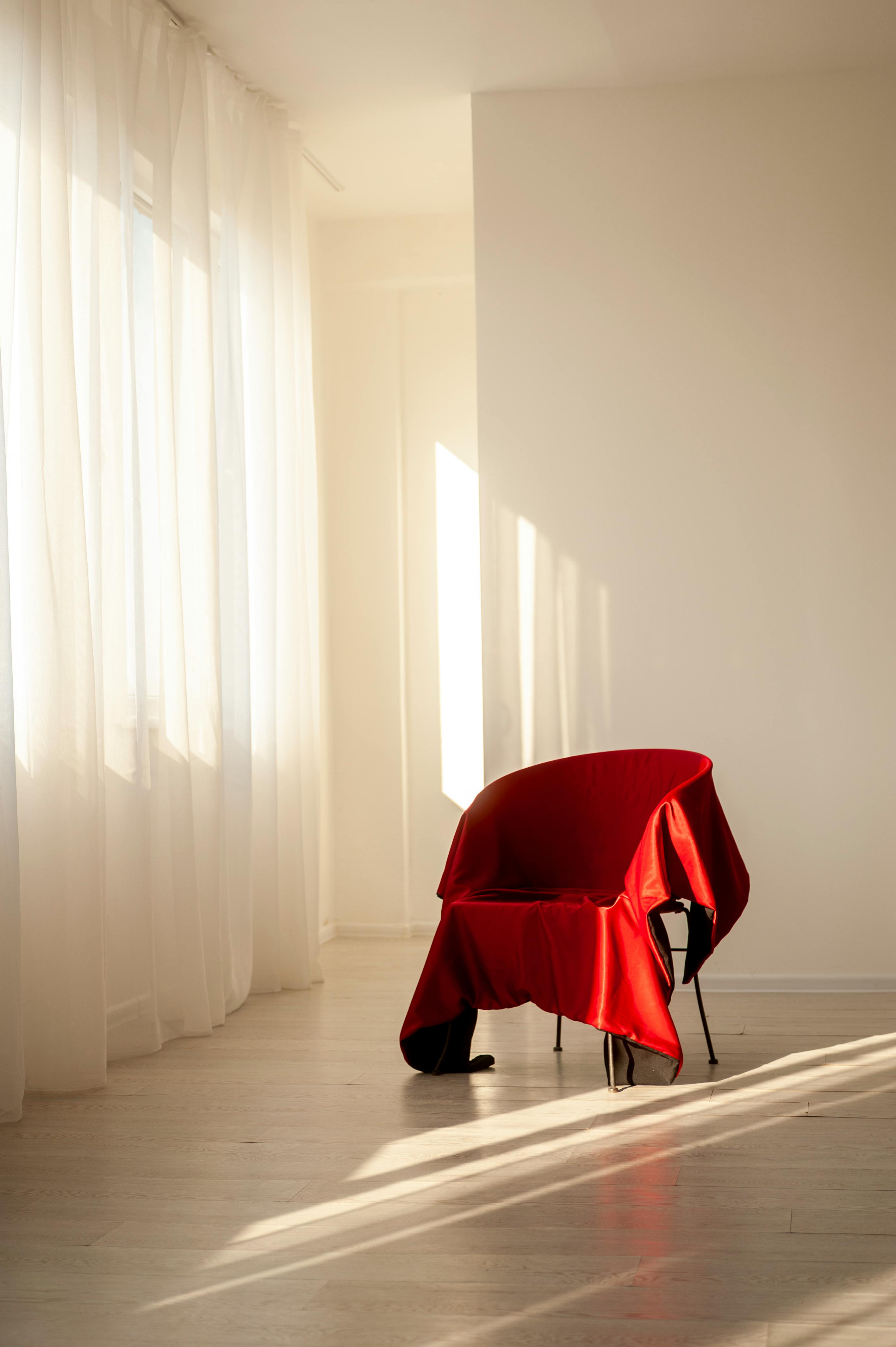 ฟรี ห้องสไตล์มินิมอลทันสมัยที่มีเก้าอี้สีแดงอาบแสงแดดอ่อนๆ ผ่านม่านโปร่ง คลังภาพถ่าย