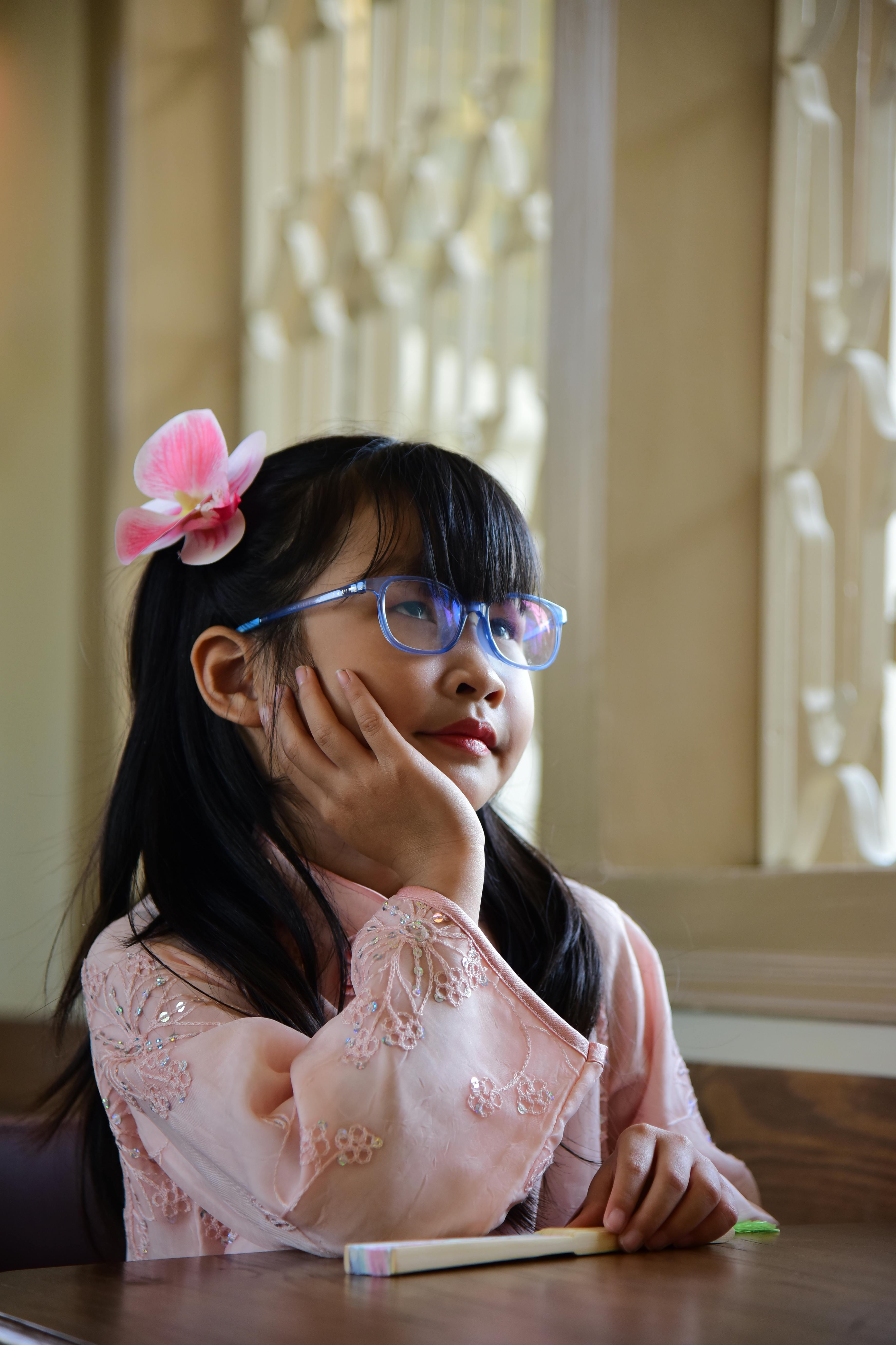 Gratis Ung pige i briller og lyserødt tøj sidder tankefuld indendørs ved et vindue. Lagerfoto